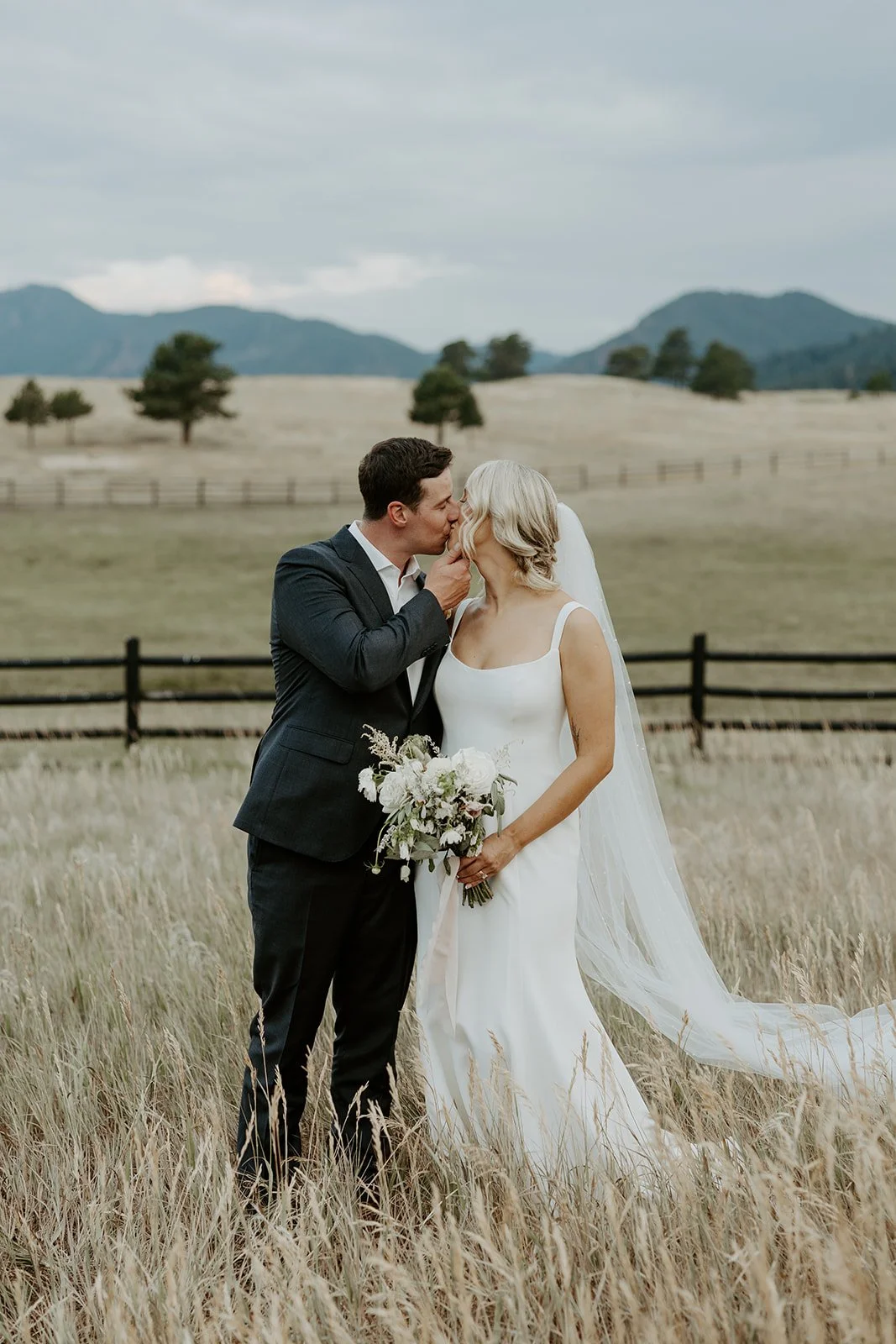 A couple kissing while taking wedding photos in a field