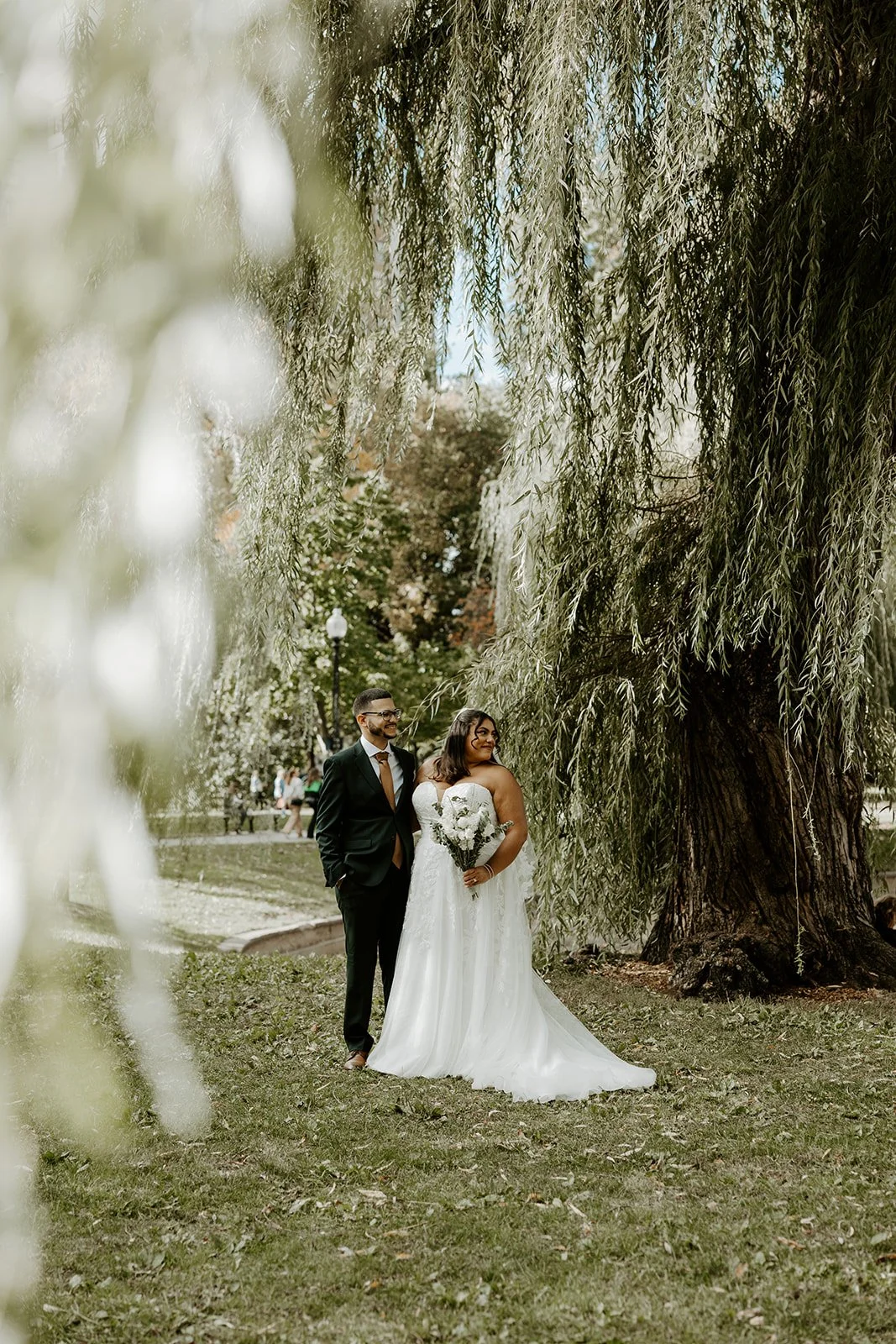 A bride and groom posing for wedding photos in front of a willow tree