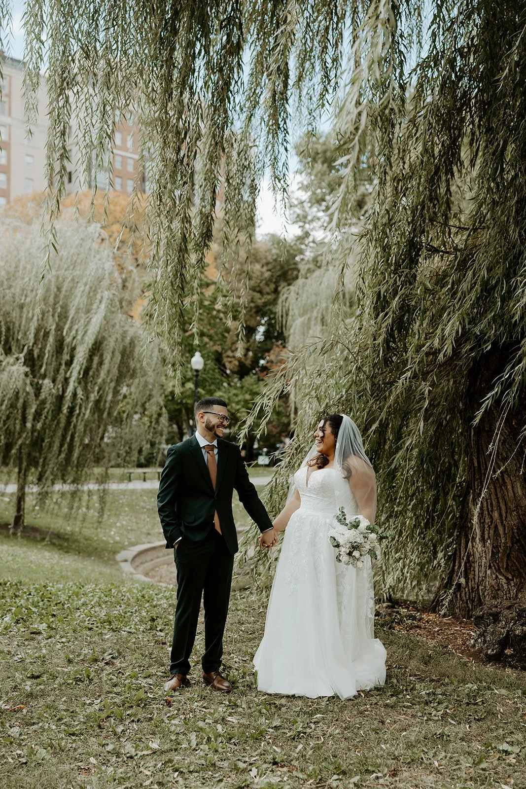 A bride and groom posing for wedding photos in front of a willow tree