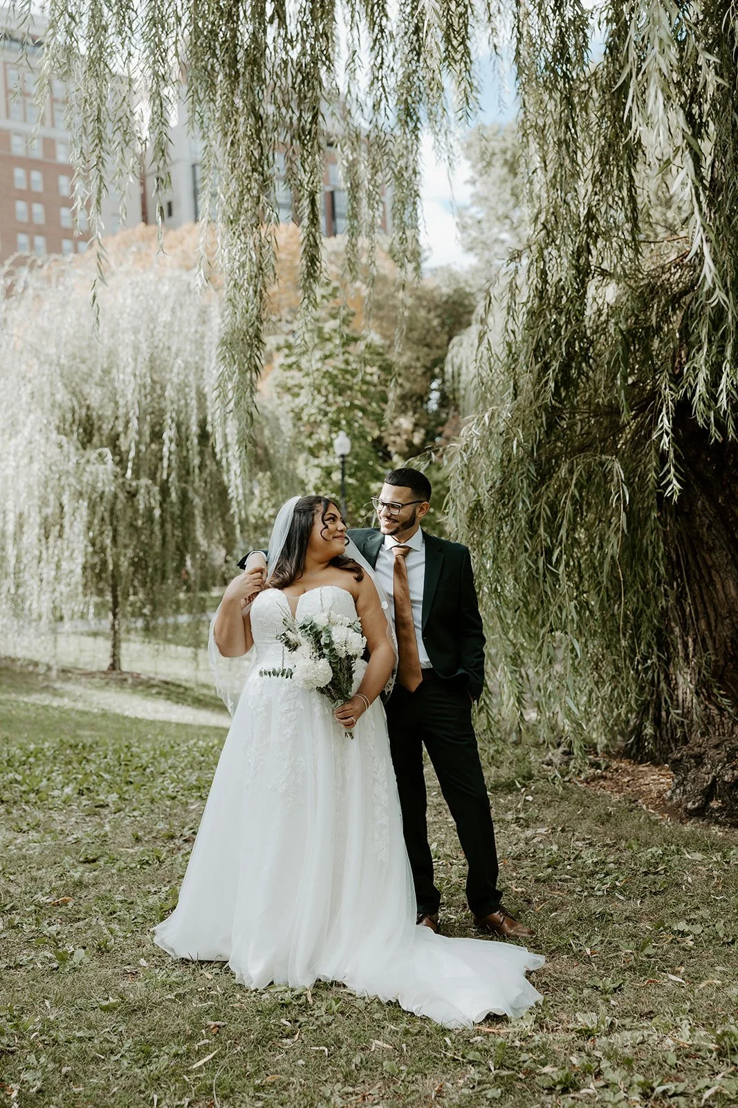 A bride and groom posing for wedding photos in front of a willow tree