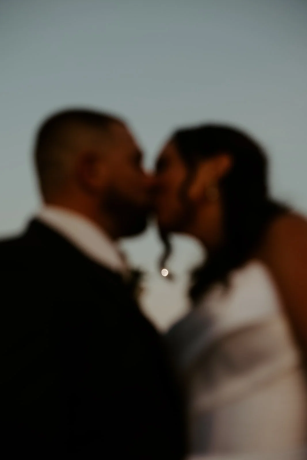 A bride and groom kissing in front of the moon