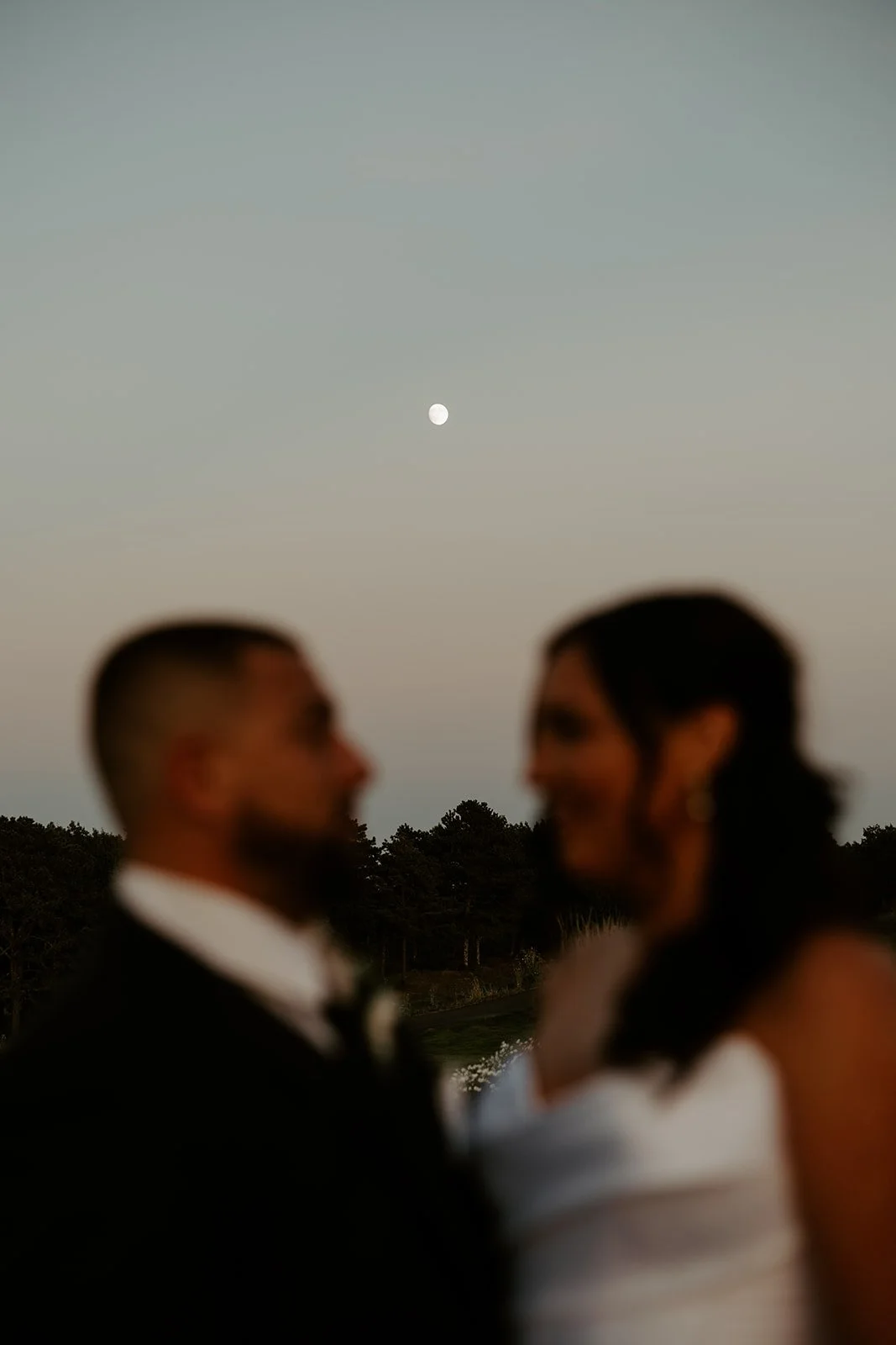 A bride and groom kissing in front of the moon