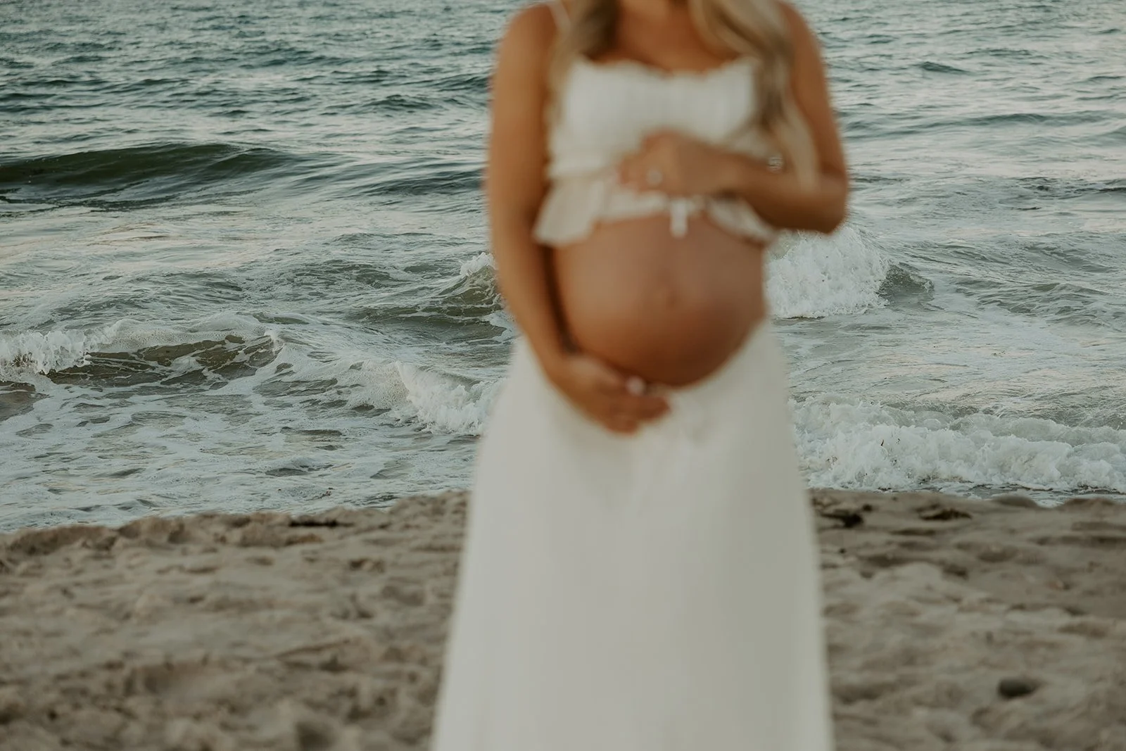 A picture of a woman holding her baby bump from beach maternity photos