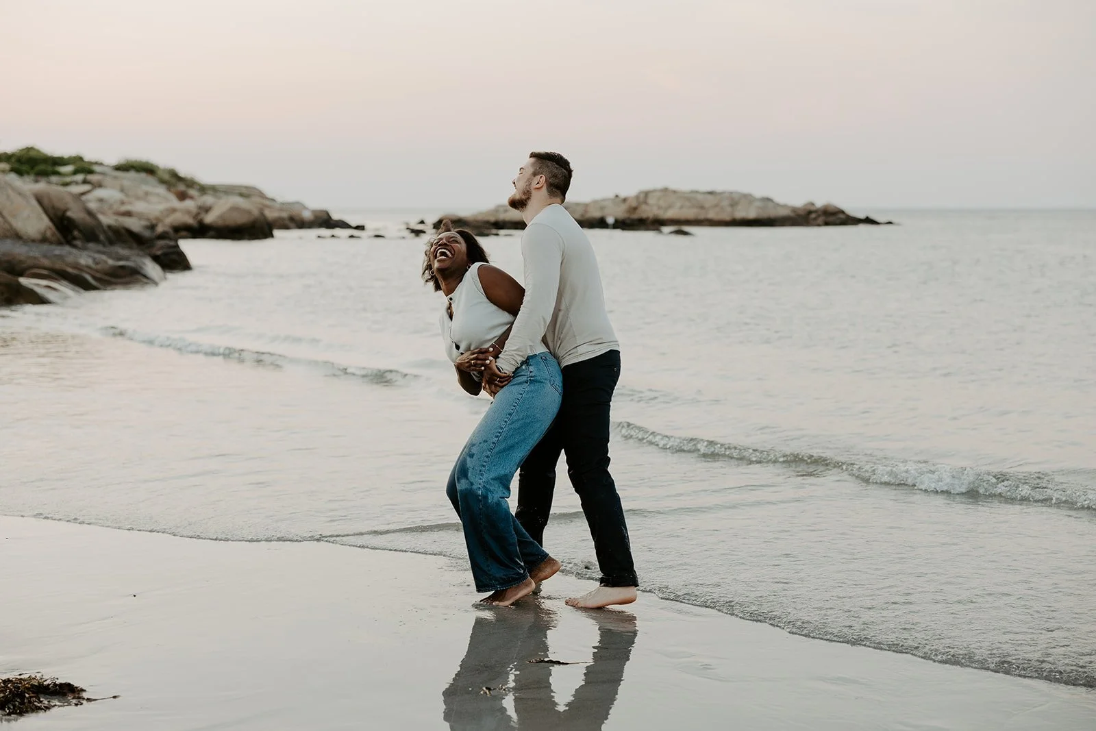 A couple laughing during a beach engagement photoshoot