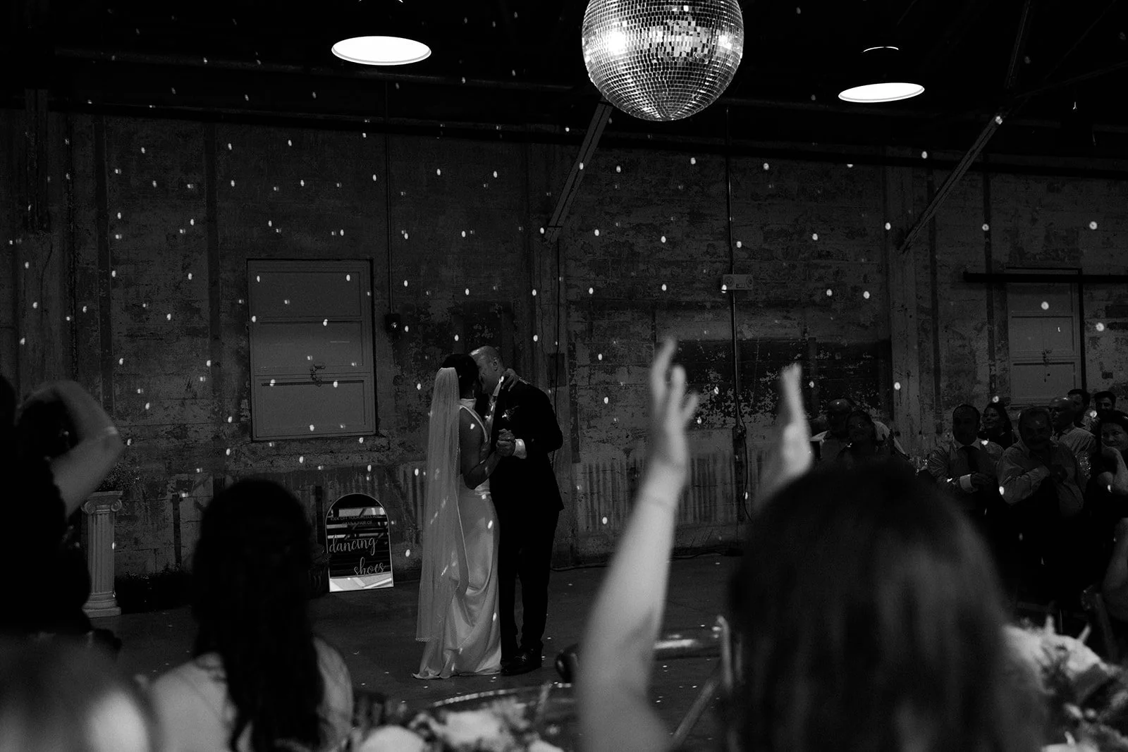 A black and white candid of wedding guests dancing underneath a disco ball
