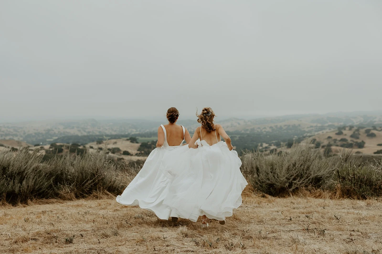 Two brides running through a field at their whimsical wedding