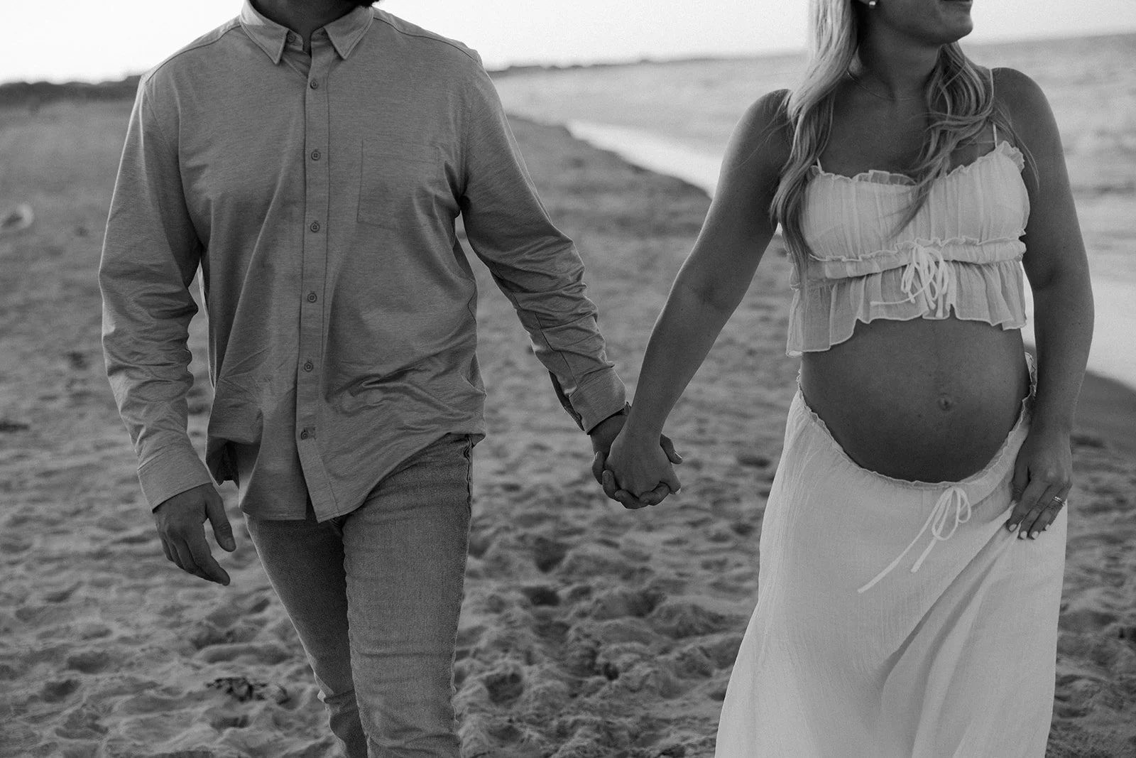 A couple holding hands on the beach for maternity photos