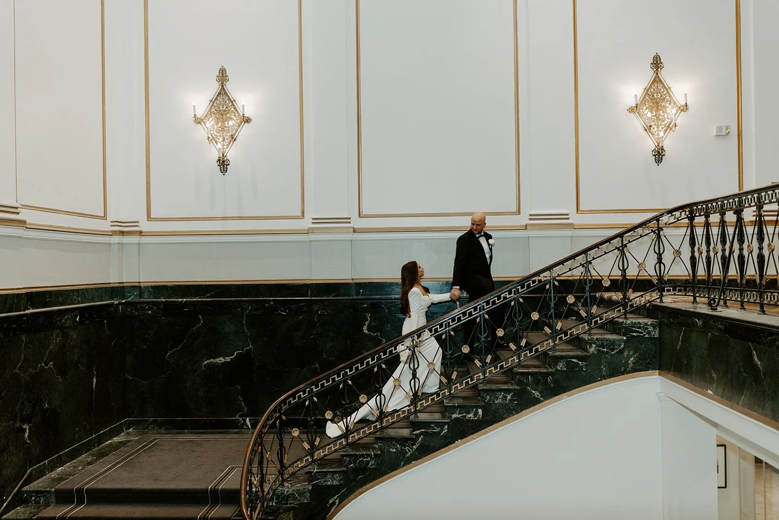 A bride and groom walking up the stairs in their indoor wedding venue for an off season wedding