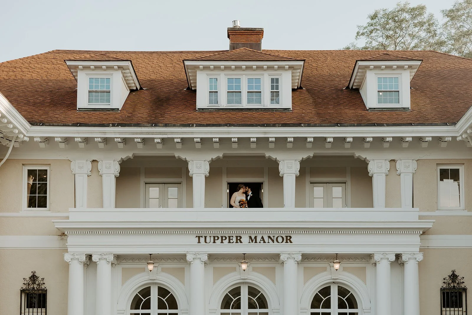 A bride and groom kissing on the balcony of an estate wedding venue