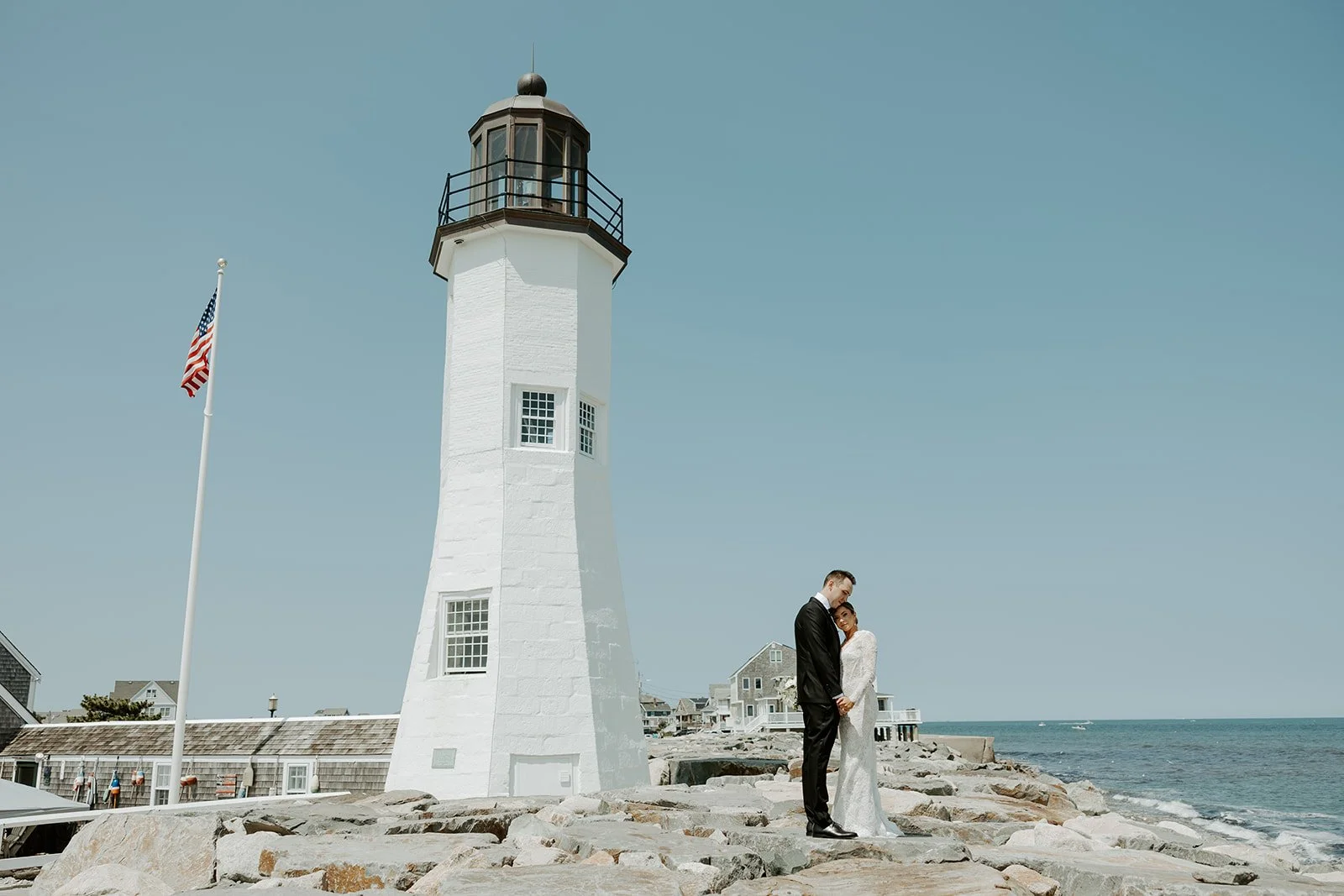 A bride and groom posign for wedding photos beside a lighthouse in boston