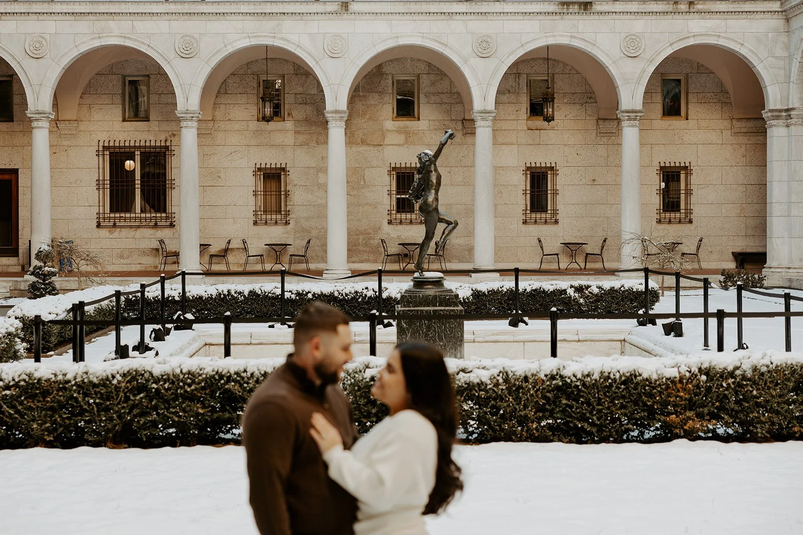A couple posing for Boston Public Library engagement photos in front of snow at the Boston public library