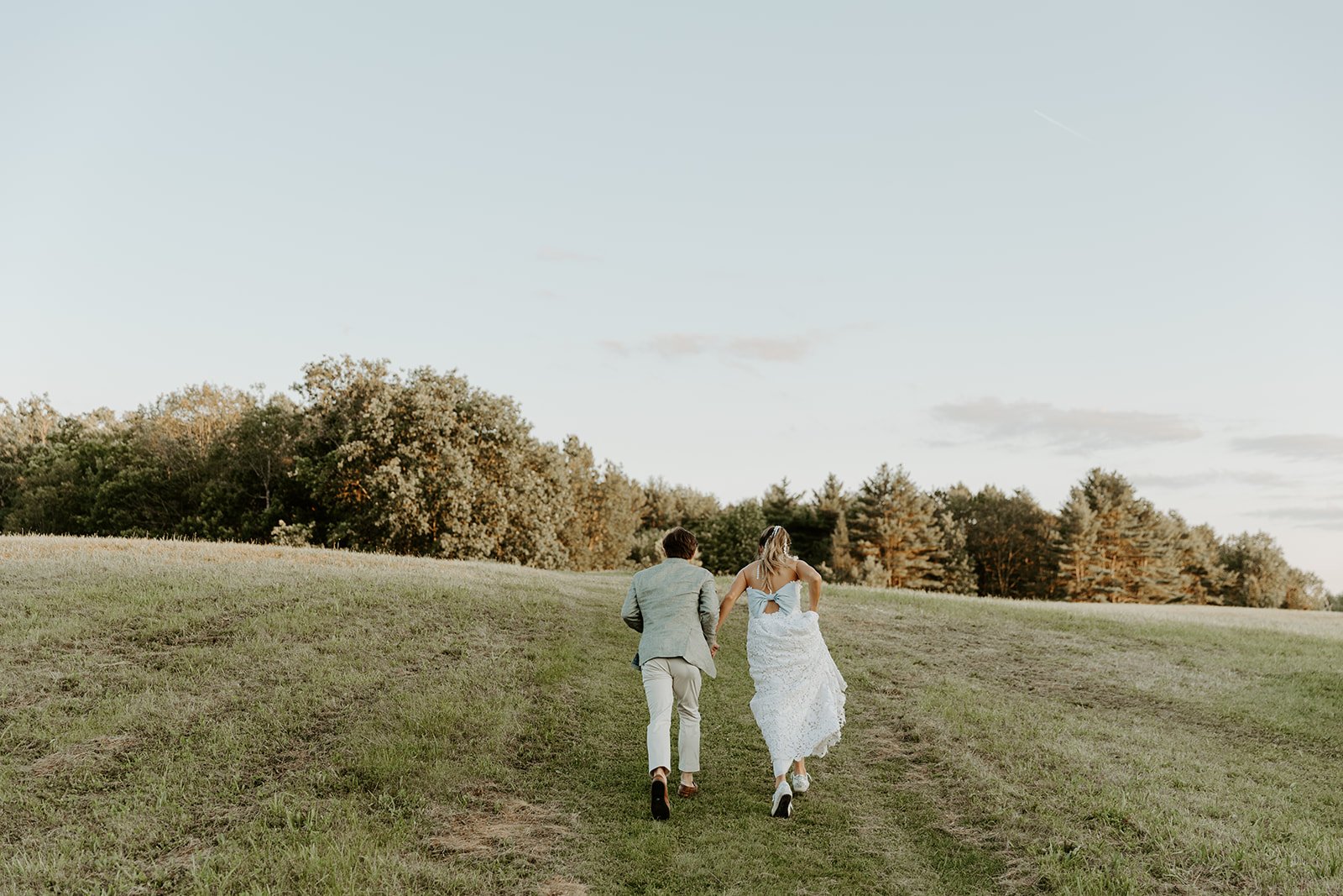 A bride and groom running through a field