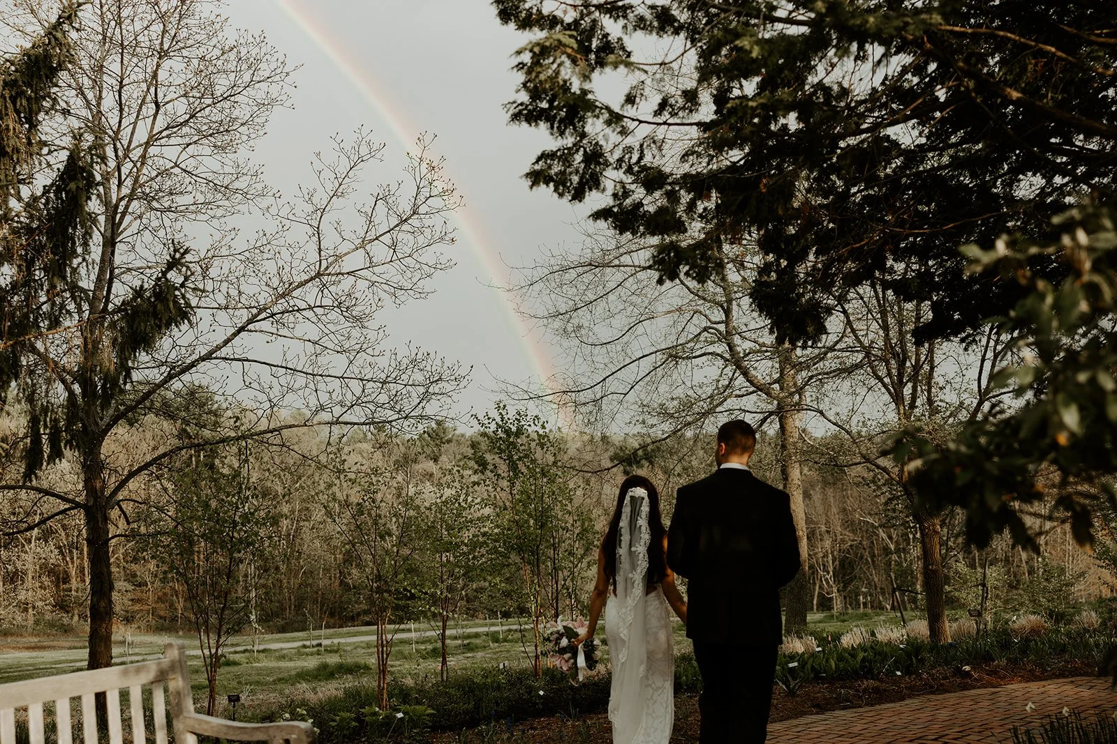 A bride and groom taking wedding photos with a rainbow