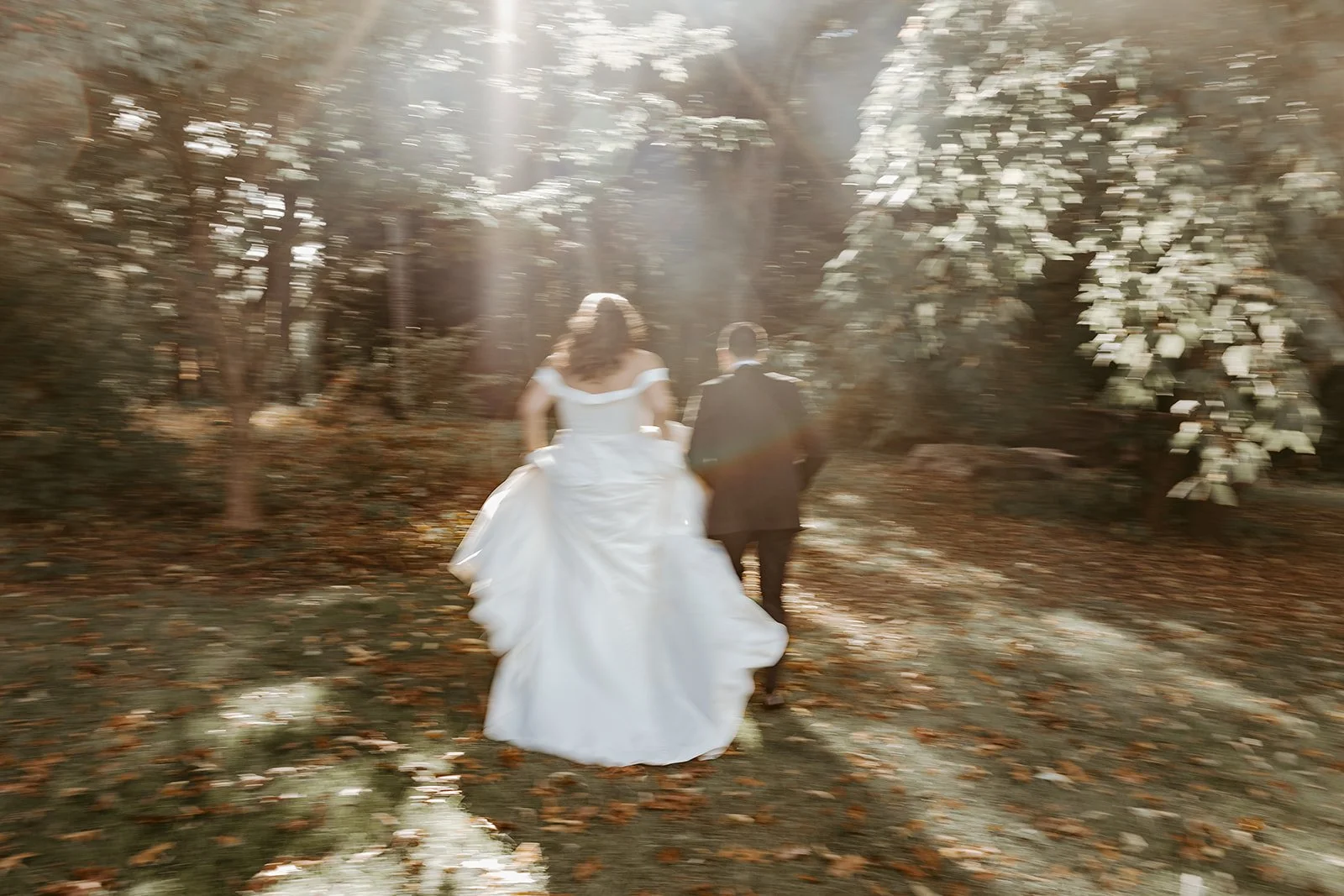A bride and groom running towards the woods for wedding photos