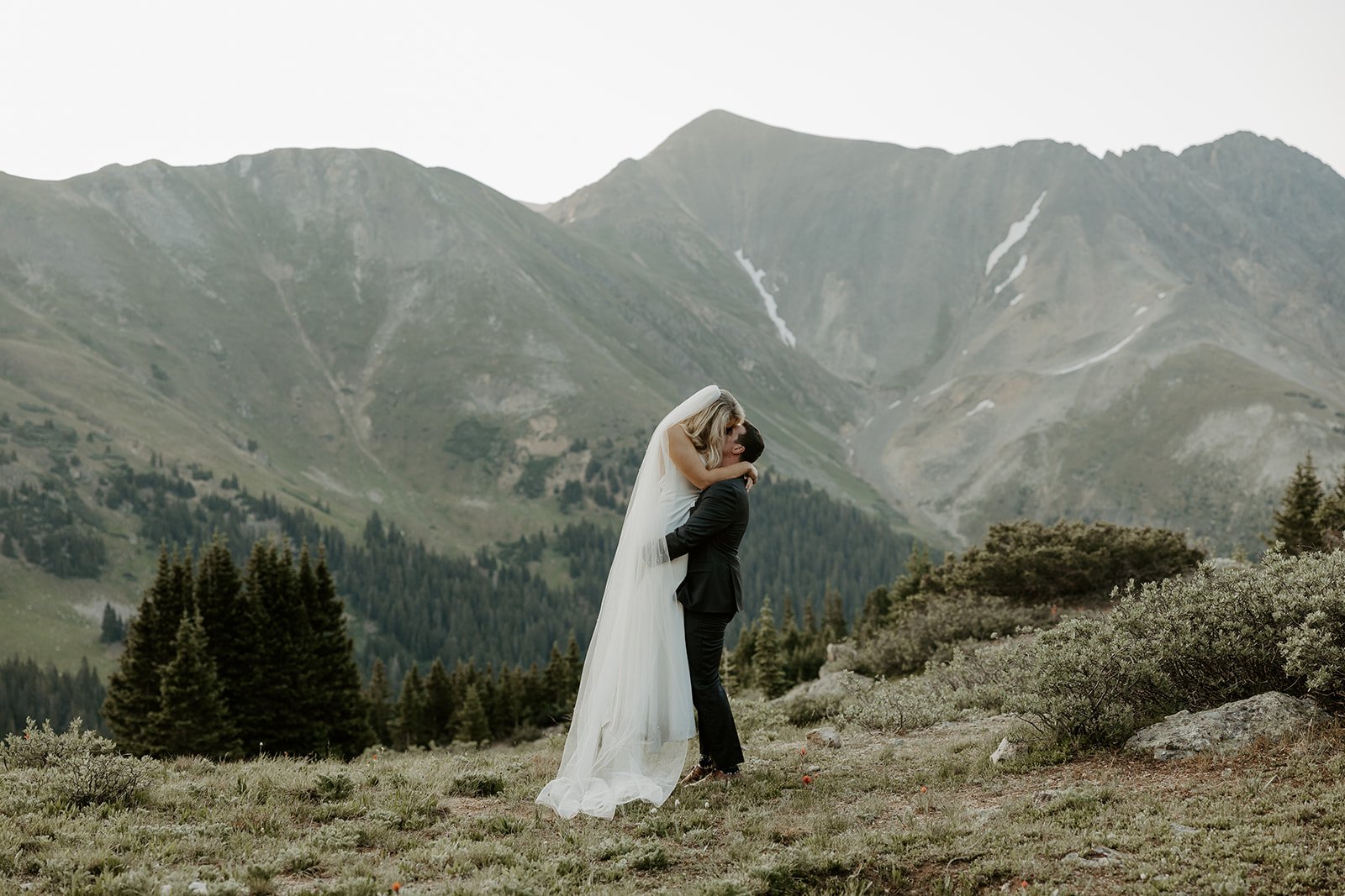 A bride and groom kissing in front of a mountain range
