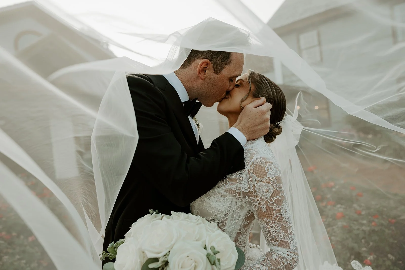 A bride and groom kissing underneath a veil