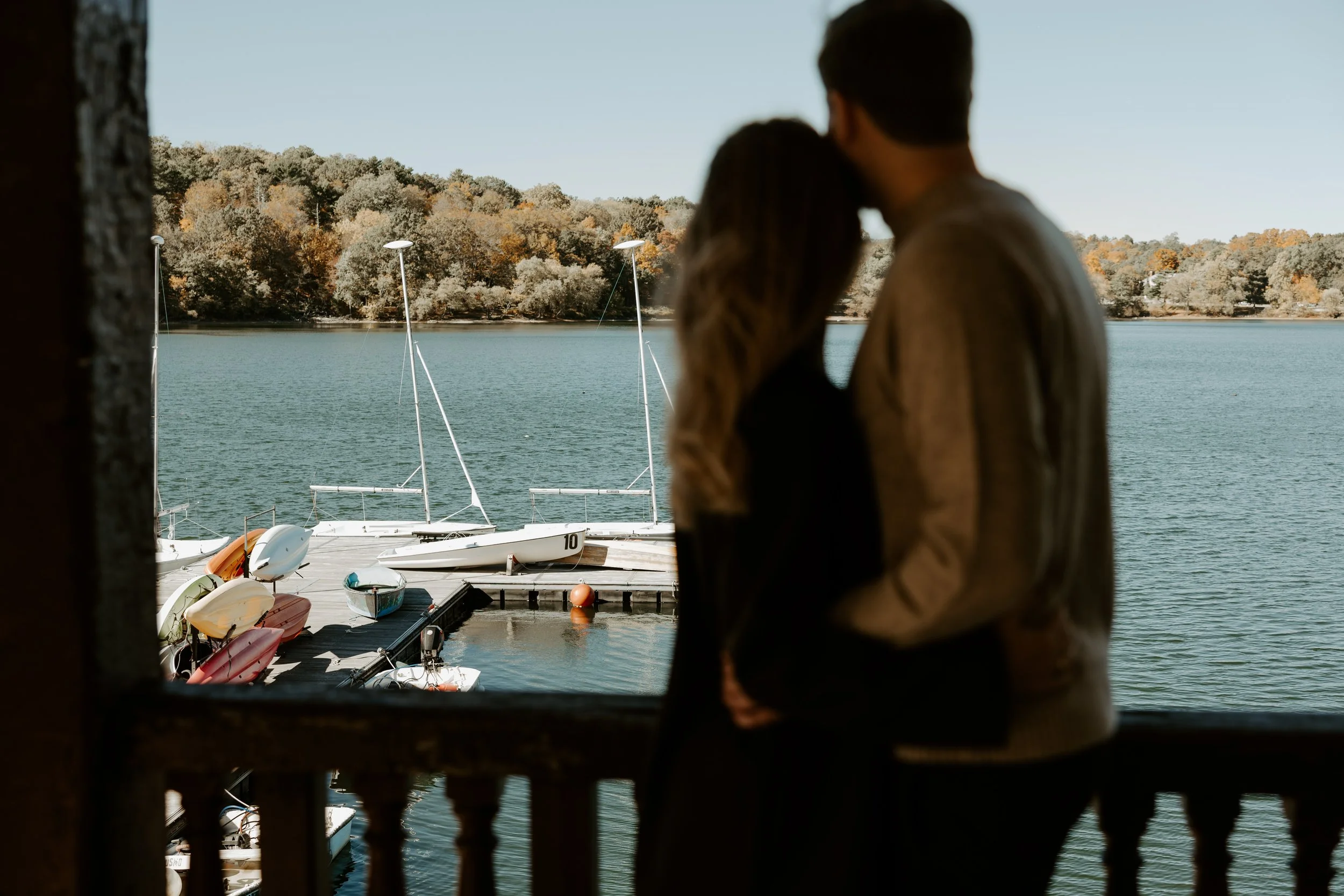 A unique engagement photo with sailboats in the background captured by a Boston engagement photographer
