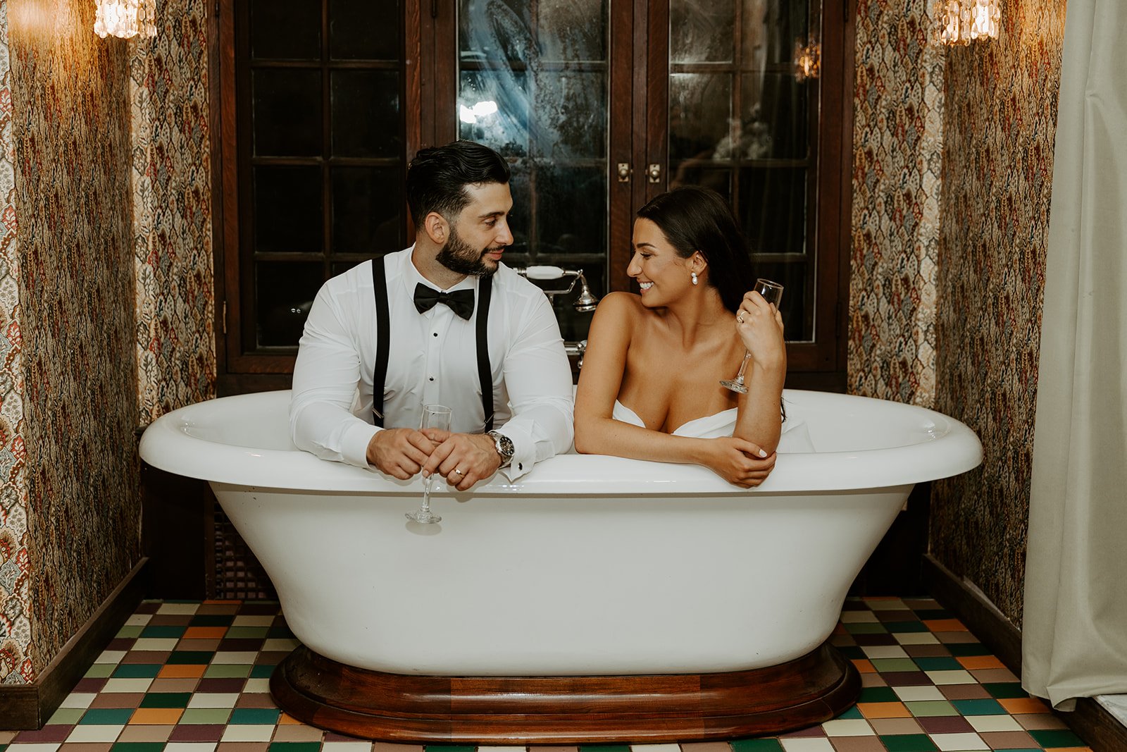 A bride and groom taking wedding photos in a clawfoot bathtub