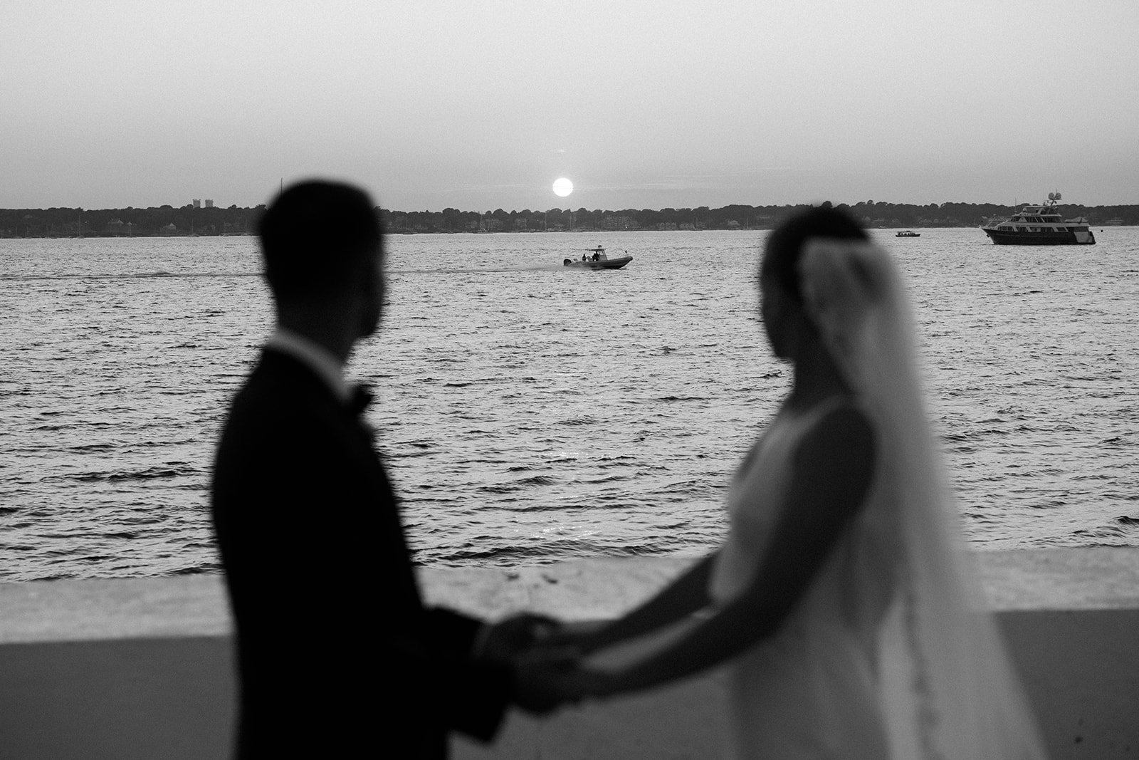A black and white photo of a bride and groom watching the sunset over the shore