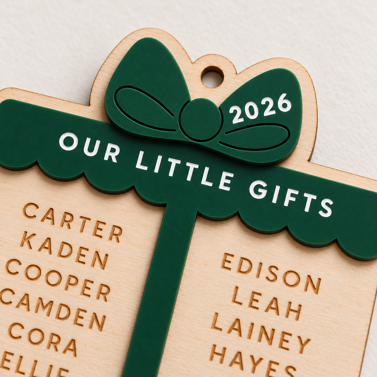 Close-up of hunter green acrylic bow, 2026 engraving and personalized names on a birch wood Little Gifts ornament.