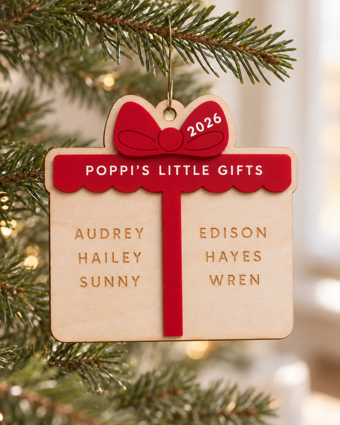 Red acrylic and birch wood ornament reading “Poppi’s Little Gifts,” personalized with six names and hanging on a Christmas tree.
