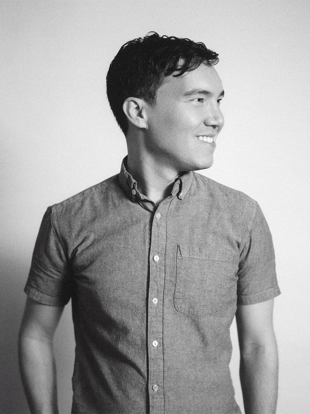 Black and white portrait of a man with short dark hair, smiling and looking to the side, wearing a button-up shirt with a pocket on the left chest.