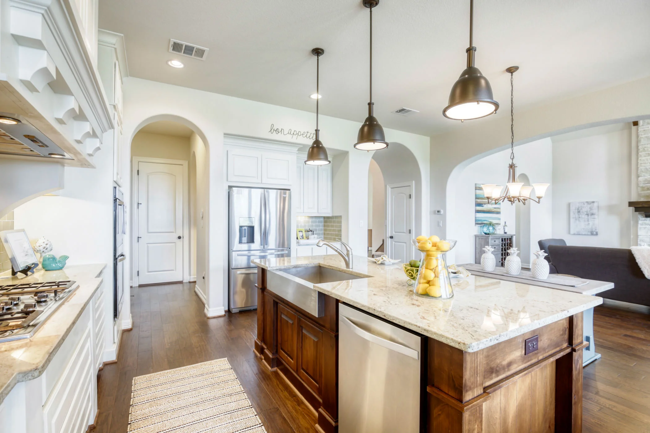 Modern kitchen with white cabinets, granite countertops, a central island with wooden cabinetry, stainless steel appliances, and pendant lighting.