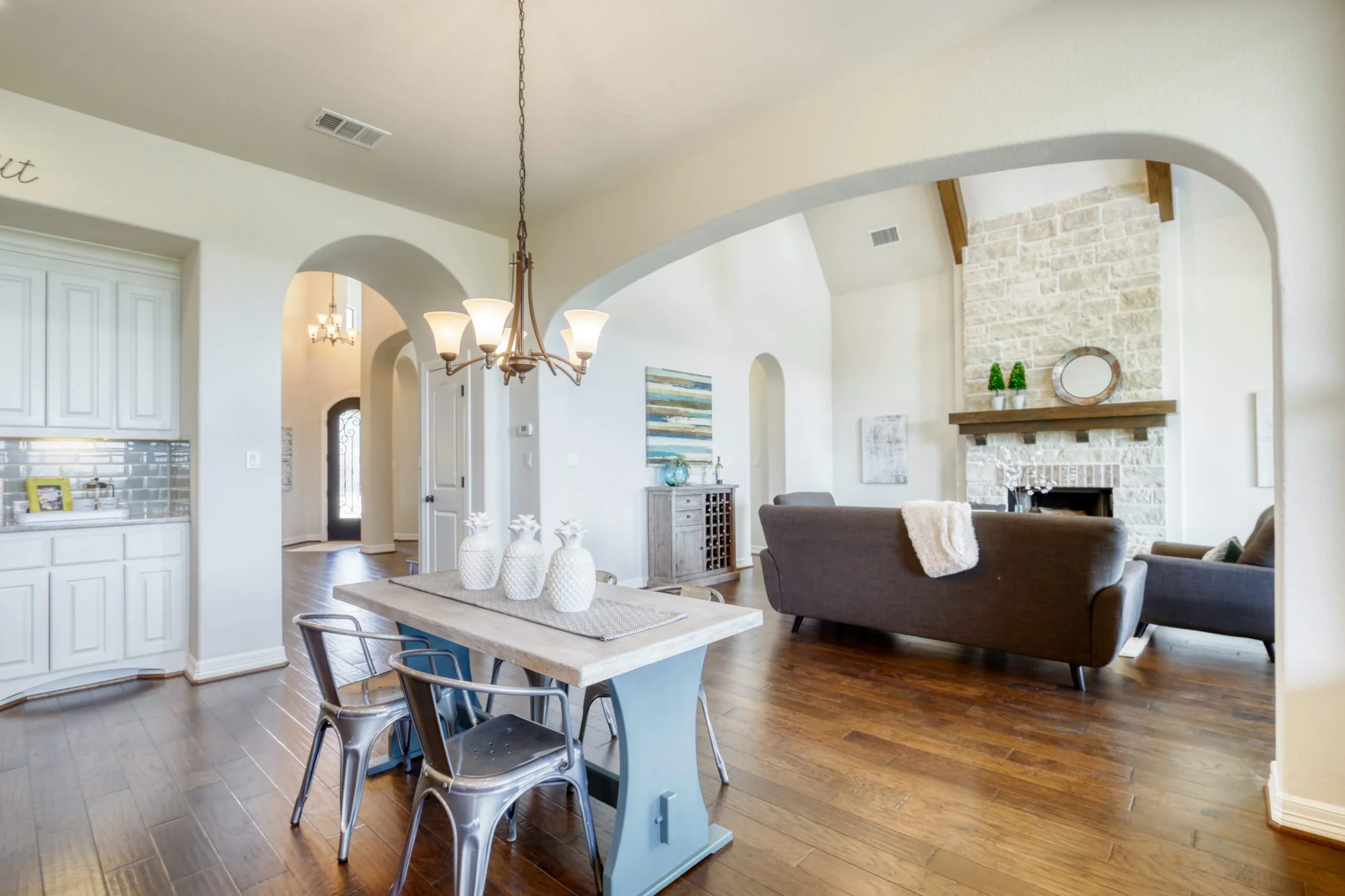 Bright modern living room and dining area with white walls, hardwood floors, a stone fireplace, and contemporary furniture.