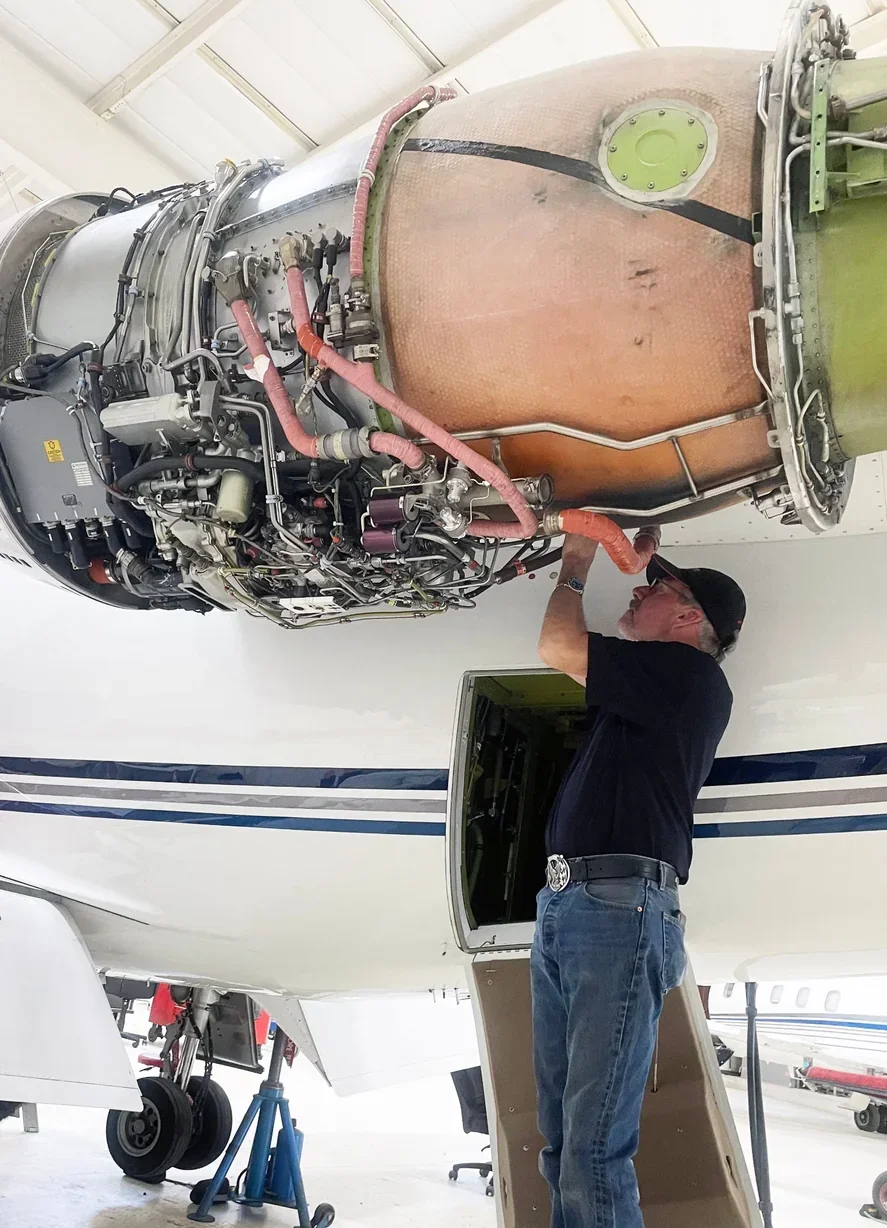 Technician on a ladder servicing a business jet engine