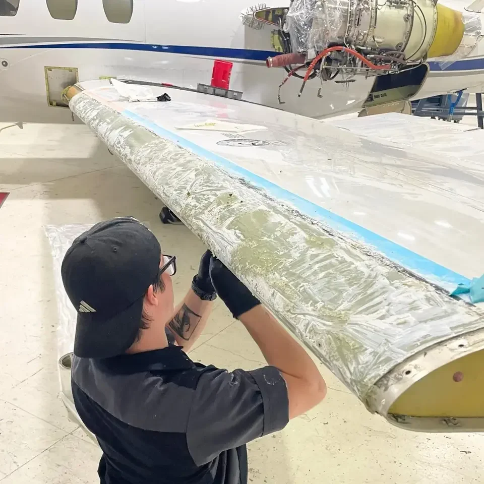 Technician removing old de-ice boot adhesive from a wing leading edge