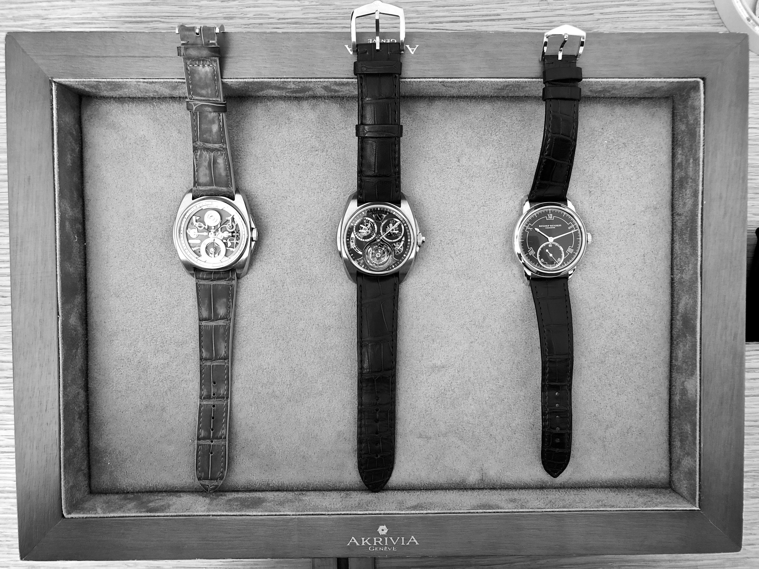 Three generations of Akrivia timepieces on a display tray. From left to right: AK-06, AK-01 Tourbillon Chronographe Monopoussoir and Chronomètre Contemporain Rexhep Rexhepi.