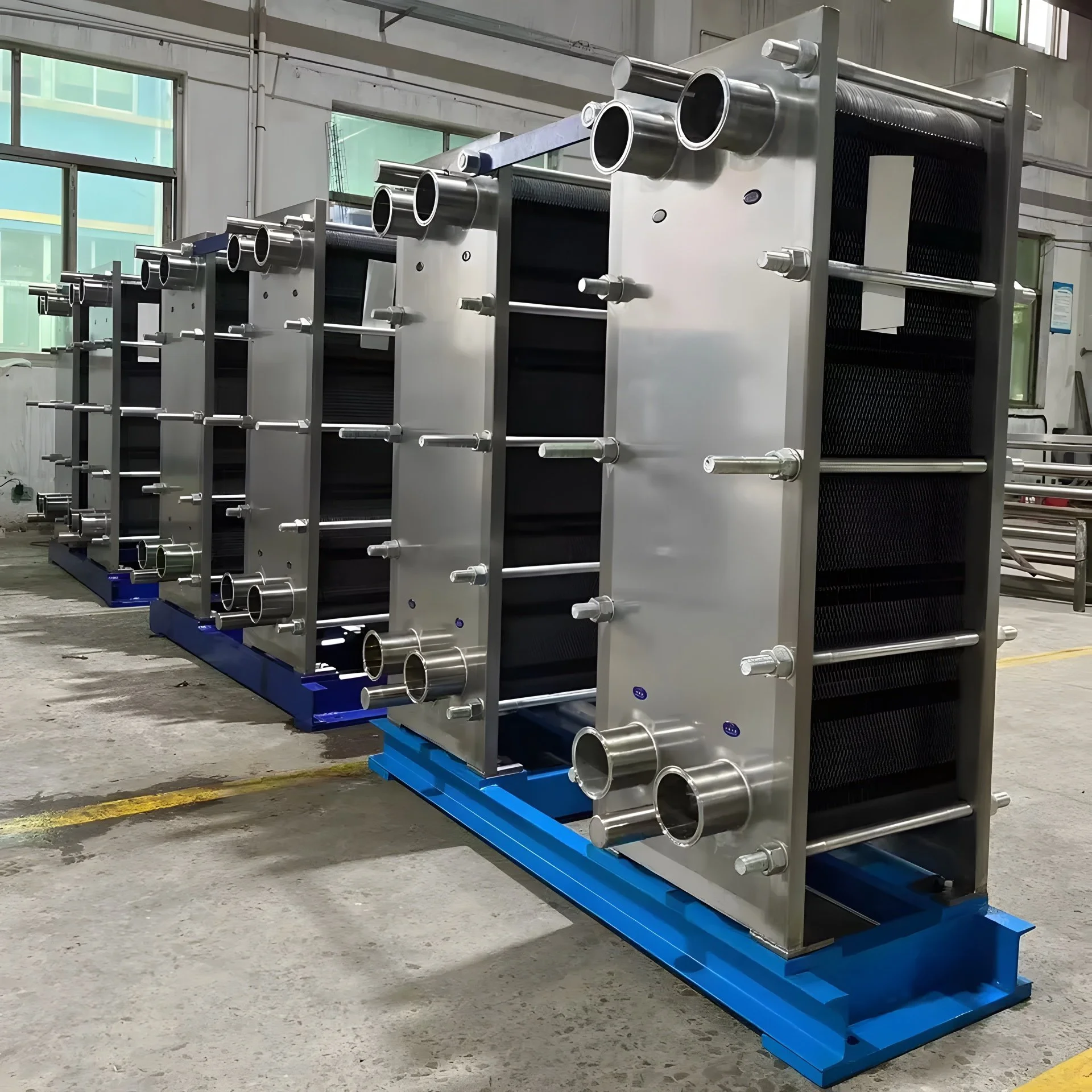 Row of large industrial heat exchangers with metal pipes in a factory setting.