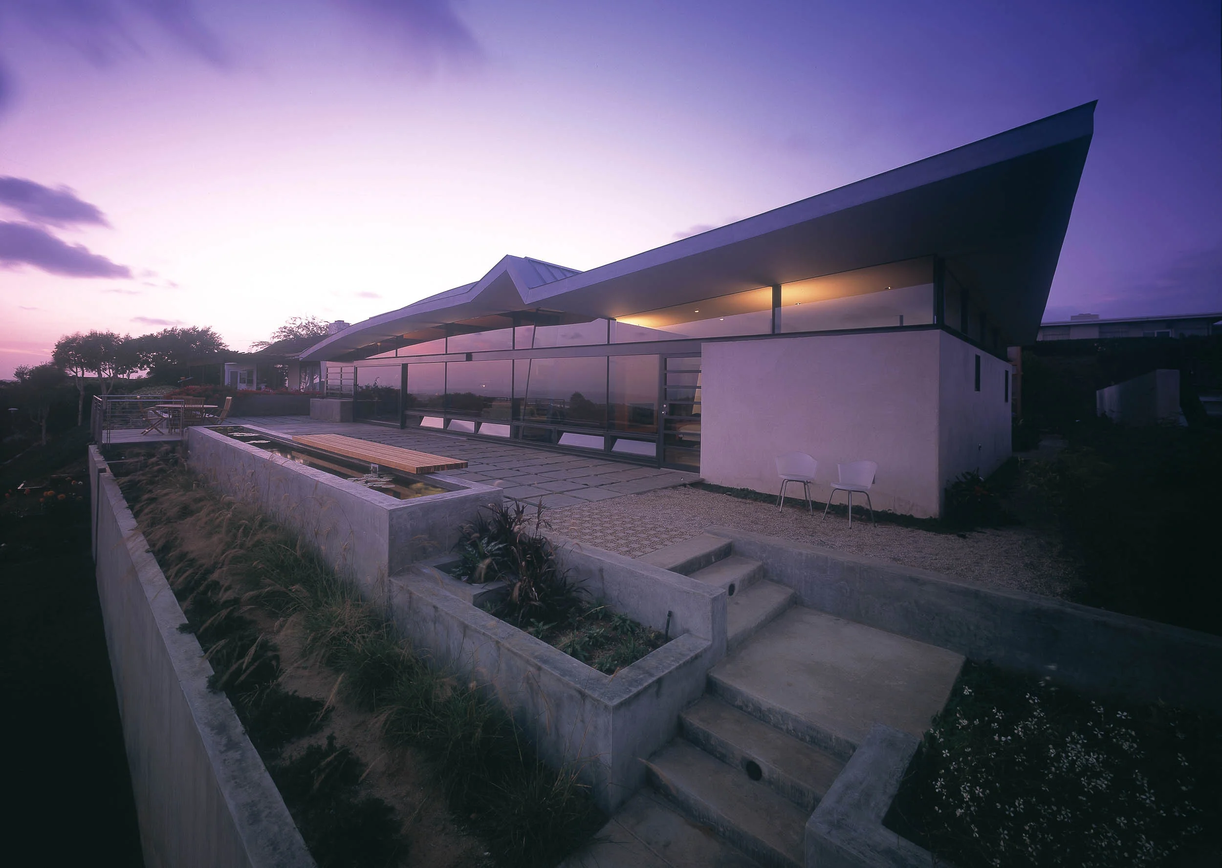 UYEMURA RESIDENCE This house employs Asian motifs to reflect the Japanese American heritage of our client. The continuous surface of an origami-like roof floats above the ground. It shapes and responds to the character of the 3 spaces it shelters: gently arcing above the great room, folding above the master bedroom suite and forming a conventional gable over the bedroom/garage wing. Shoji-like garage doors 'roll' on a cantilevered steel beam. The origami roof extends into the interior forming an entry canopy. Exterior wall and ceiling materials are brought into the interior to form a seamless continuity between inside and outside. A slanted purple plaster wall divides the master bedroom from the great room in such a way as to create the illusion of a single uninterrupted volume between the two. A floor to ceiling glass wall extends along the entire length of the house opening it to the expansive ocean vista, coastline and Catalina Island and Newport Harbor. Dining and Tatami Rooms open to a walled garden, which provides outdoor privacy and an alternative to the expansive ocean vista. Operable windows at floor and ceiling on opposite sides of the great room create a natural convection and continuous cross ventilation. A radiant heated warm floor of polished concrete floor extends throughout all rooms allowing for easy maintenance as well as passive solar temperature control. Newport Beach, CA 1998 American Architecture Award, Chicago Athenaeum 1997 Los Angeles American Institute Architects Design Award 1997 Orange County American Institute Architects Merit Award 1994 Los Angeles American Institute Architects Design Award