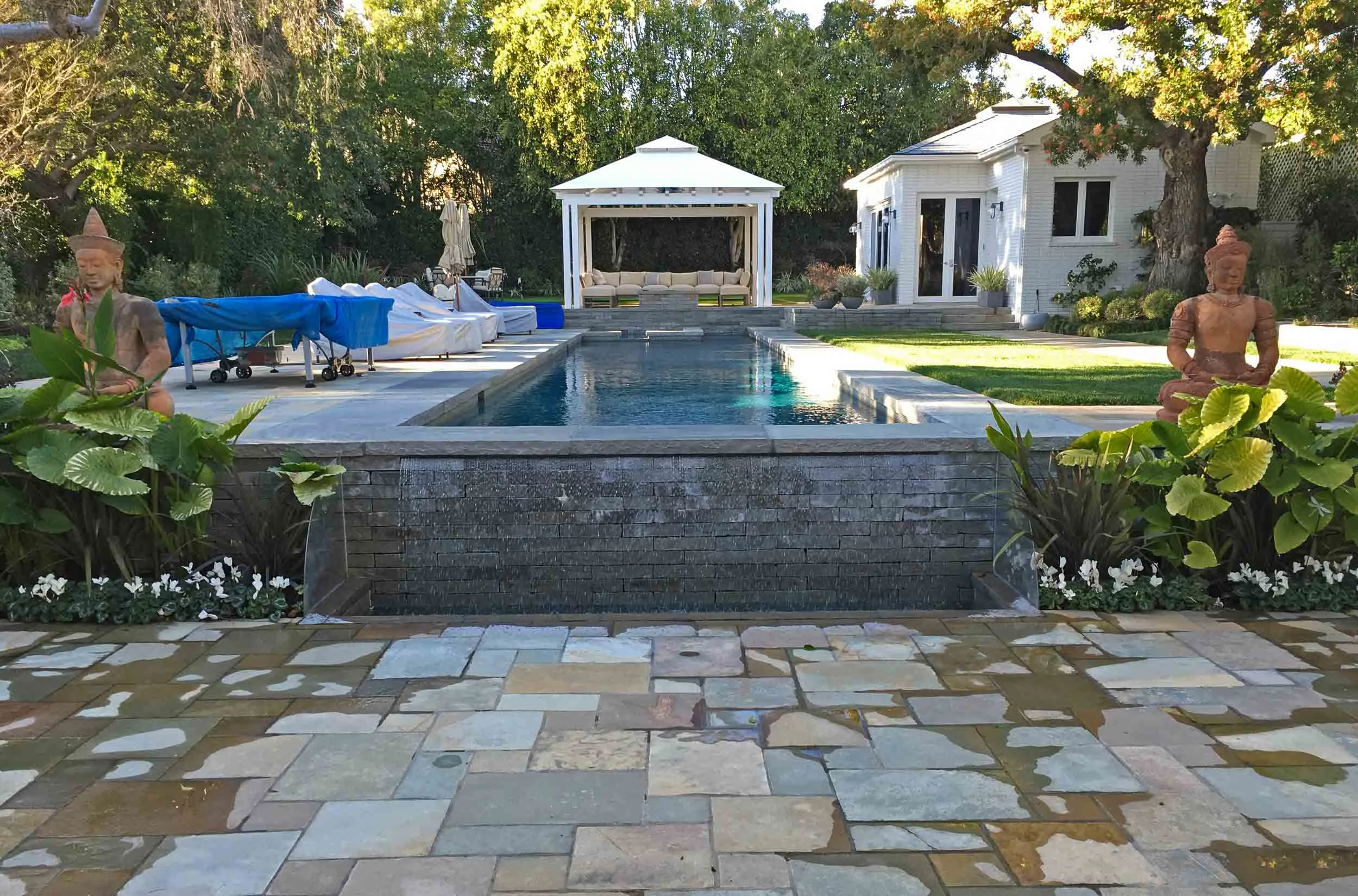 WRIGHT RESIDENCE POOL HOUSE & LANDSCAPE An existing backyard was transformed into a contemporary environment for Southern California outdoor entertaining. Granite pavers define a new enlarged rear patio, walkways and gazebo patio at the far end of the pool. The existing pool has been resurfaced, new lighting installed and and a water fall added at the short end. The existing accessory building was re-purposed into a Spa, Rec Room and Bathroom. Within the Spa is a Far-Infared Sauna, Steam Room and WC. The Rec Room is clad in hand-selected Koa wood paneling. The Fireplace-TV is bordered by hand-rubbed steel paneling and hand-blown glass light fixtures. A large Nana-Wall door opens this room to the gazebo-patio which centers around a fire pit. White fabric shades the gazebo. A custom fabricated glass chandelier hangs from the gazebo center. Brentwood CA