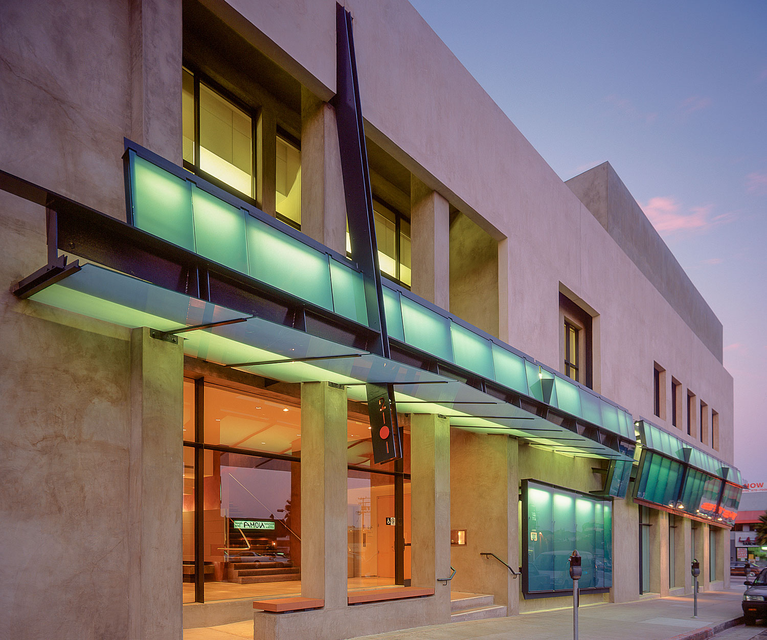 UNIVERSITY OF SANTA MONICA This building is home to an institution offering graduate programs in Spiritual Psychology which are presented in large group format. The school provides a psychological environment within which to enhance the experience of Self illumination. The University required a complete remodel to its facility consisting of a new facade, two new large seminar rooms for 80 and 200 students and a major reconfiguration of the interior in order to provide better circulation. The design reflects the nature of spiritual learning in the way it symbolically evokes illumination, embraces creative tension, and reflects the qualities of balance, peace, and harmony. Furthermore, the design strives for a clear expression of each part, such that each part is a whole unto itself, yet simultaneously a part of the greater Whole. A floating plane of limestone colored stucco enfolds the existing facade, unifying the existing disparities and lack of cohesion. On top of this stucco plane, a steel and glass canopy wraps the building and transforms itself into a protective awning over the entry. Inside, light from above descends into the building's center directly over the main stair. A frosted, curved, acrylic sheet suspended above this stair, is both light fixture and sculpture. The experience of ascending and descending is made ceremonial. In the two large seminar rooms, self-illumination is given symbolic expression in ceilings that open to the sky. These rooms convey both a sense of expansion and intimacy, creating a serene environment supportive of the inner work of upliftment. The larger seminar room focuses on a circular skylight that expands into an asymmetrical cone which intersects a curved wood ceiling. Suspended within this cone, a large, sculptural, translucent panel is used as a light diffuser. A sky lit vault also dominates the smaller seminar room, adding height and light to the room. Angled acoustic panels turn up into this vault as translucent, curved, light diffusers add a delicate counterpoint to the opaque, angular planes. Santa Monica, CA 1998 Los Angeles AIA Interior Architecture Honor Award
