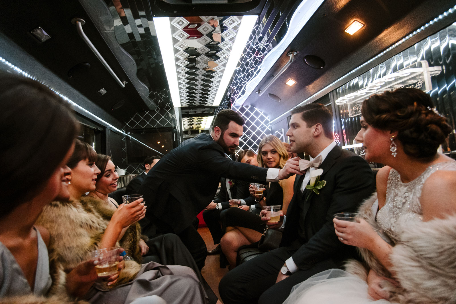 Groomsman helps groom with his tie in a limo