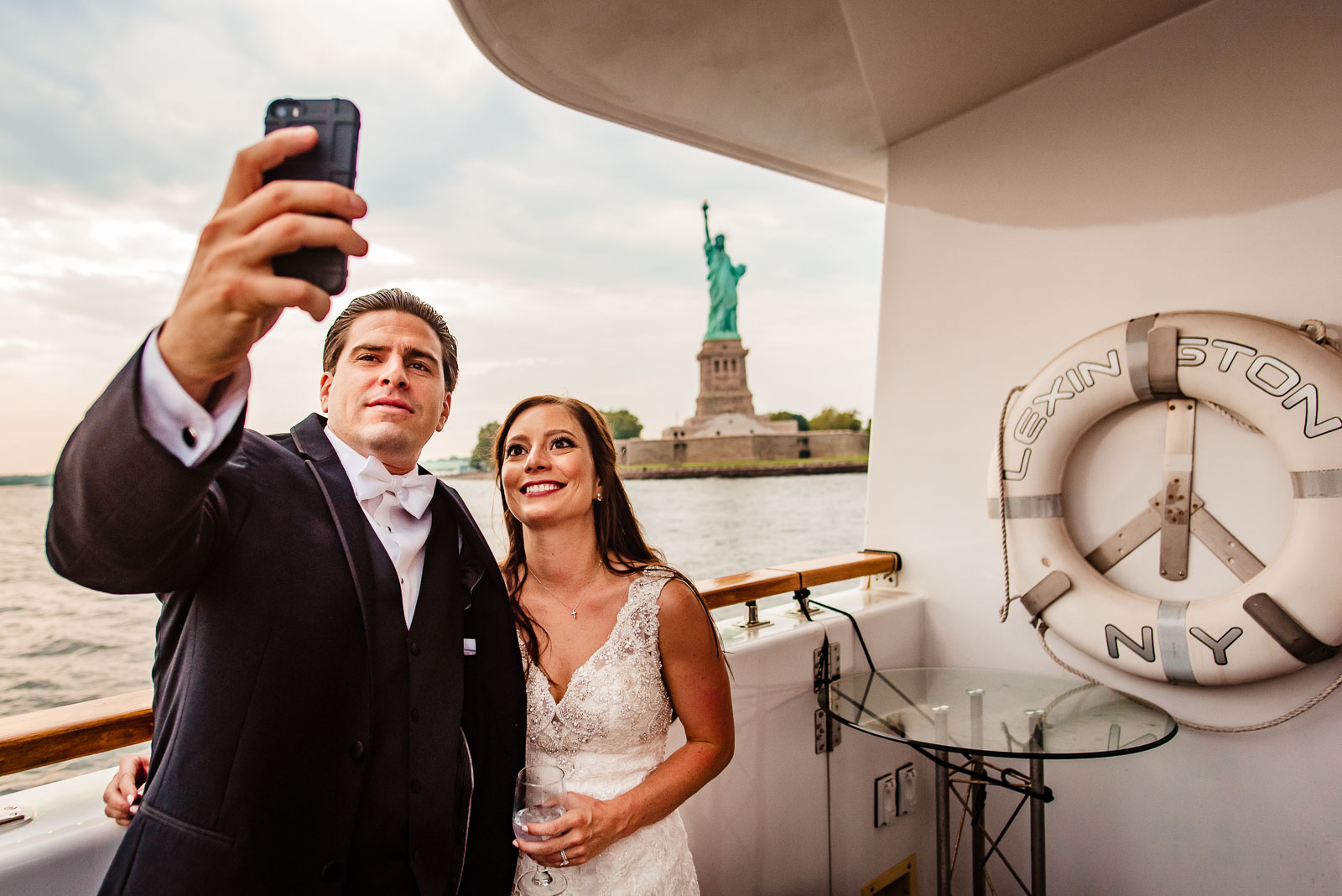 bride and groom take selfie with statue of liberty 