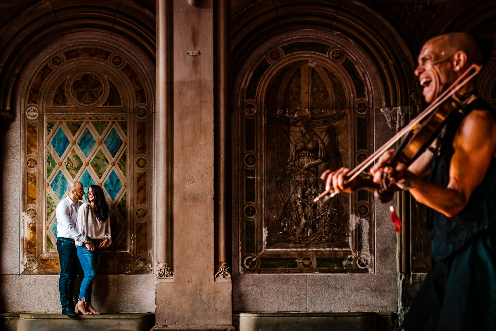 Couple laughs at bethesda terrace arch while street performer plays