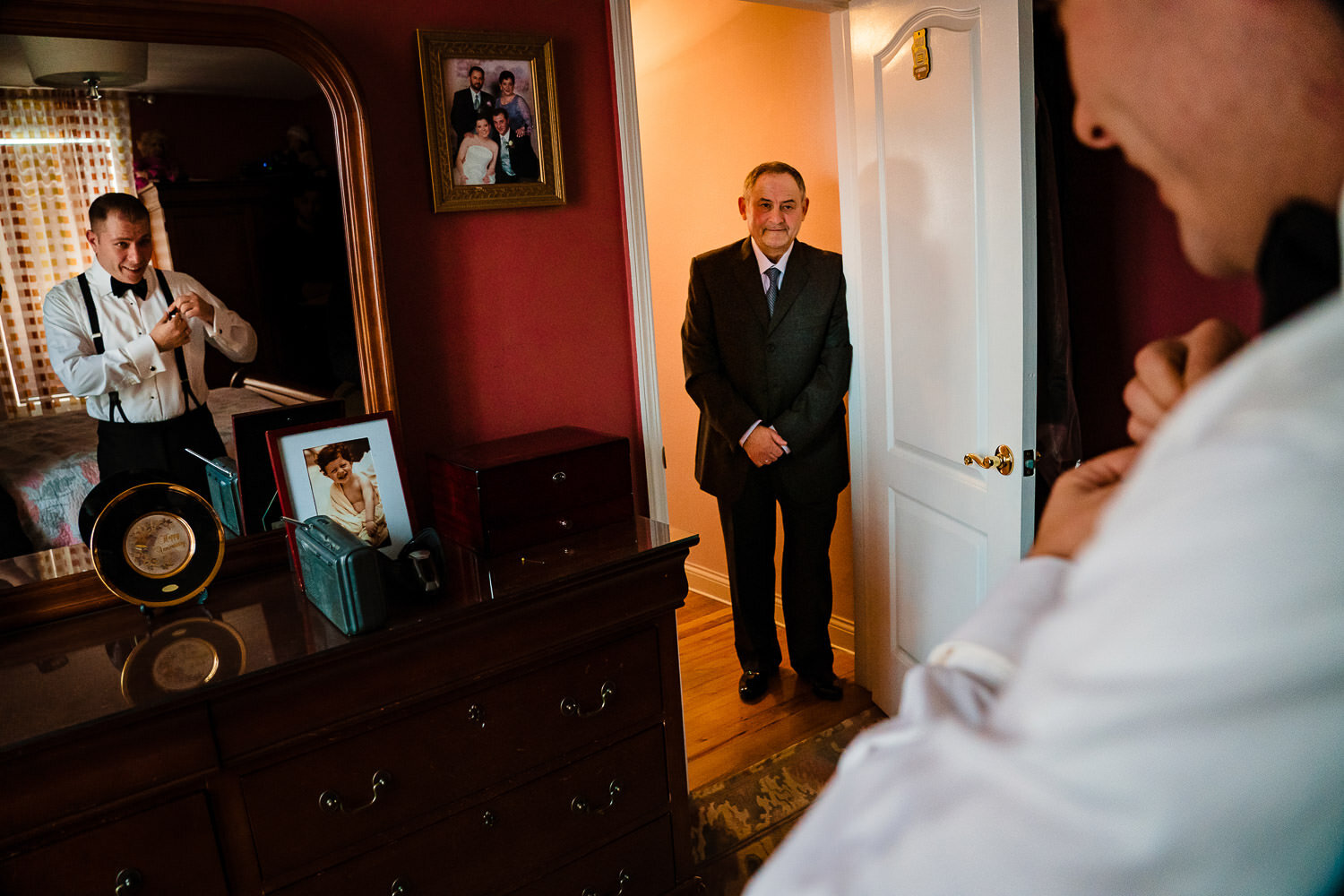Groom's father looks as his son puts on a tie in front of a mirror