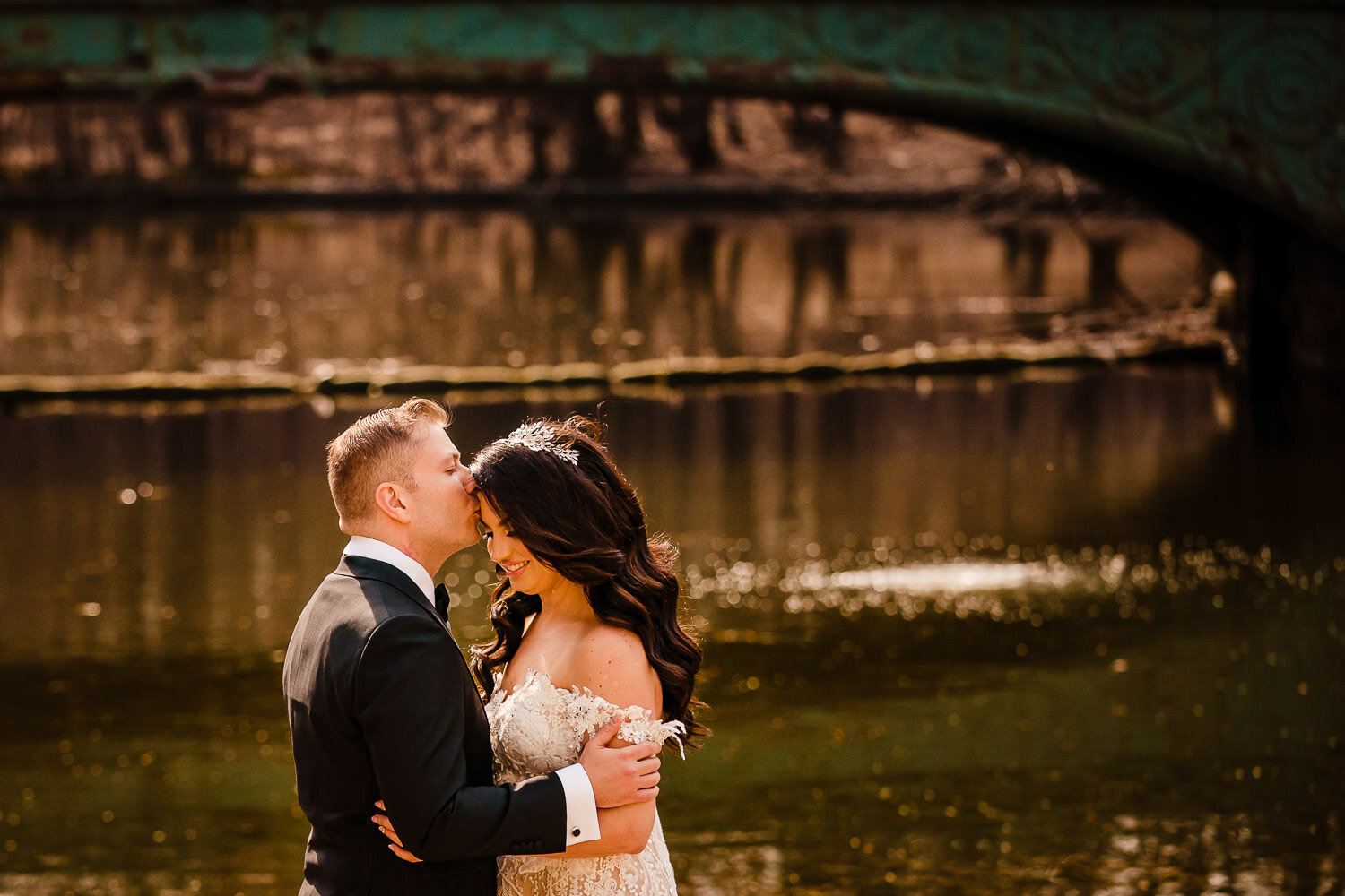 Groom kisses bride by a bridge at Prospect Park