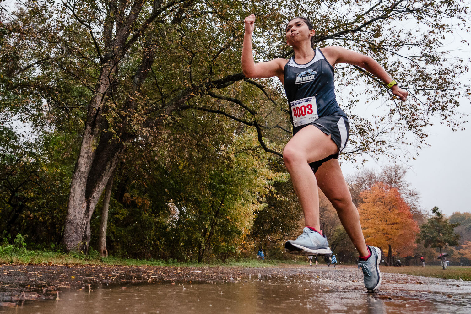 Baruch runner jumps over puddle during CUNYAC Championship race at van cortlandt park