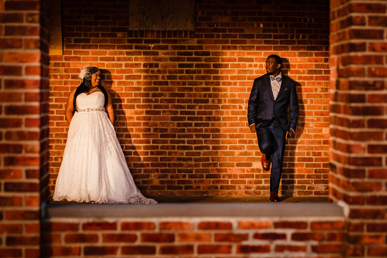 Bride and groom look at each other by red brick wall in Morgan Memorial Park in Glen Cove 