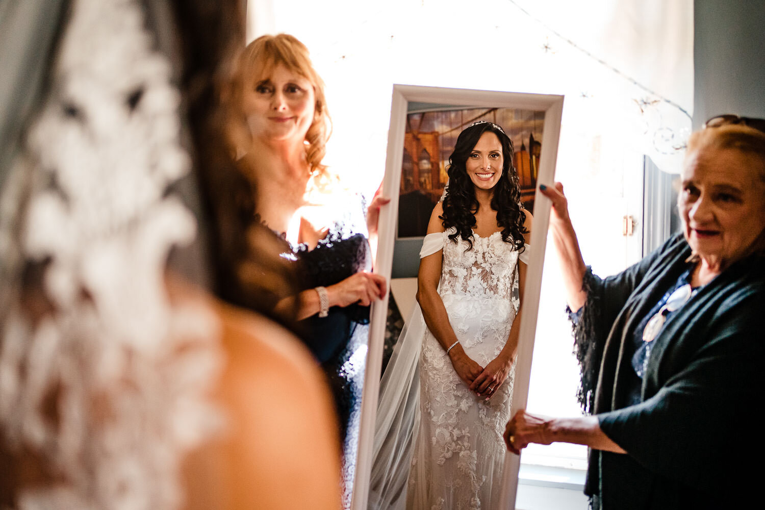 Bride looks at the mirror hald by her mother and grandmother