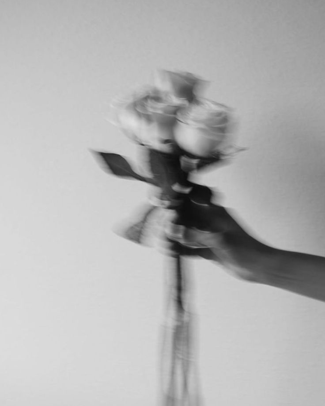 A black and white blurred photo of a hand holding a bouquet of flowers with roses, against a plain background.