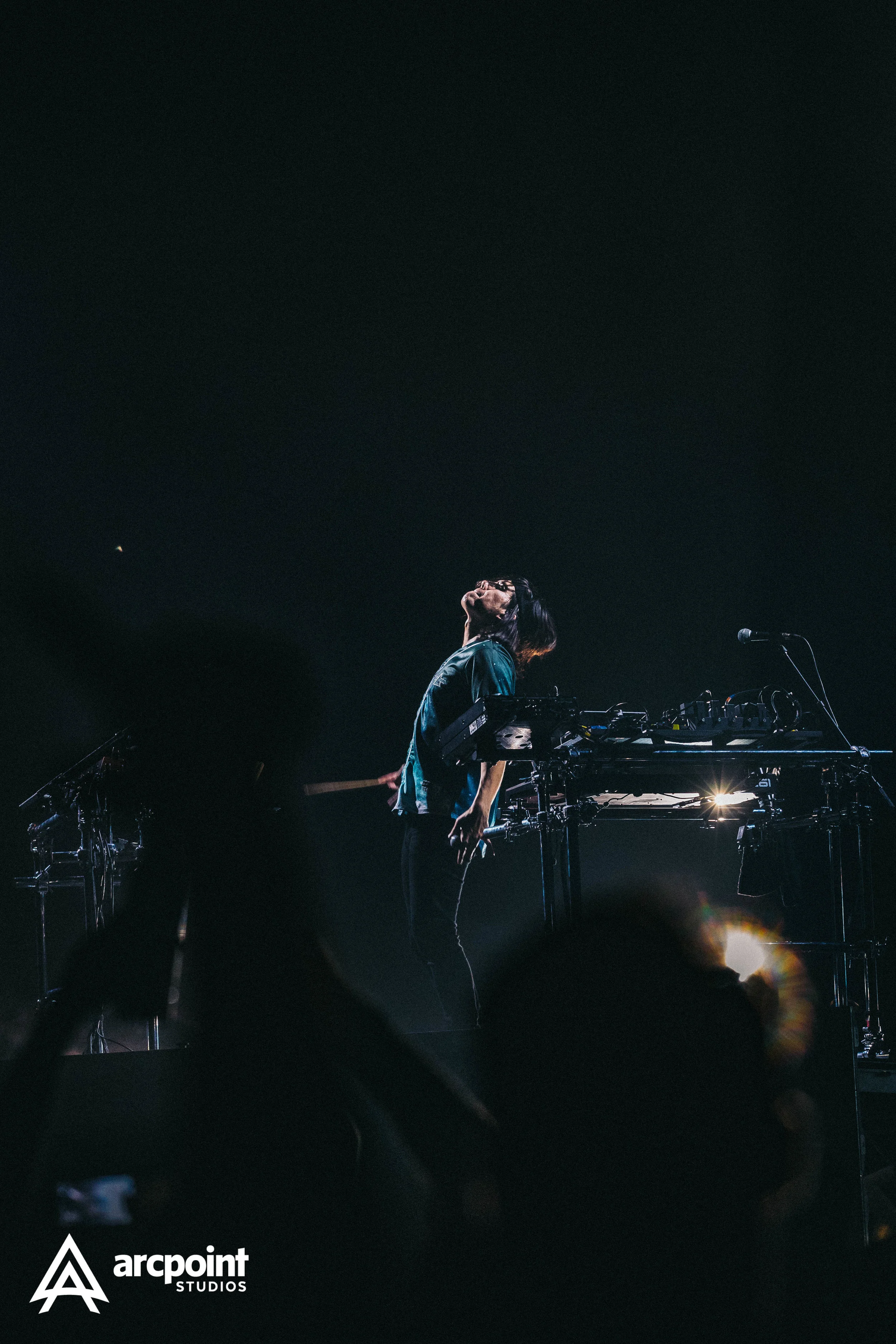 A musician on stage with electronic instrument setup, head tilted back, dark background, stage lighting