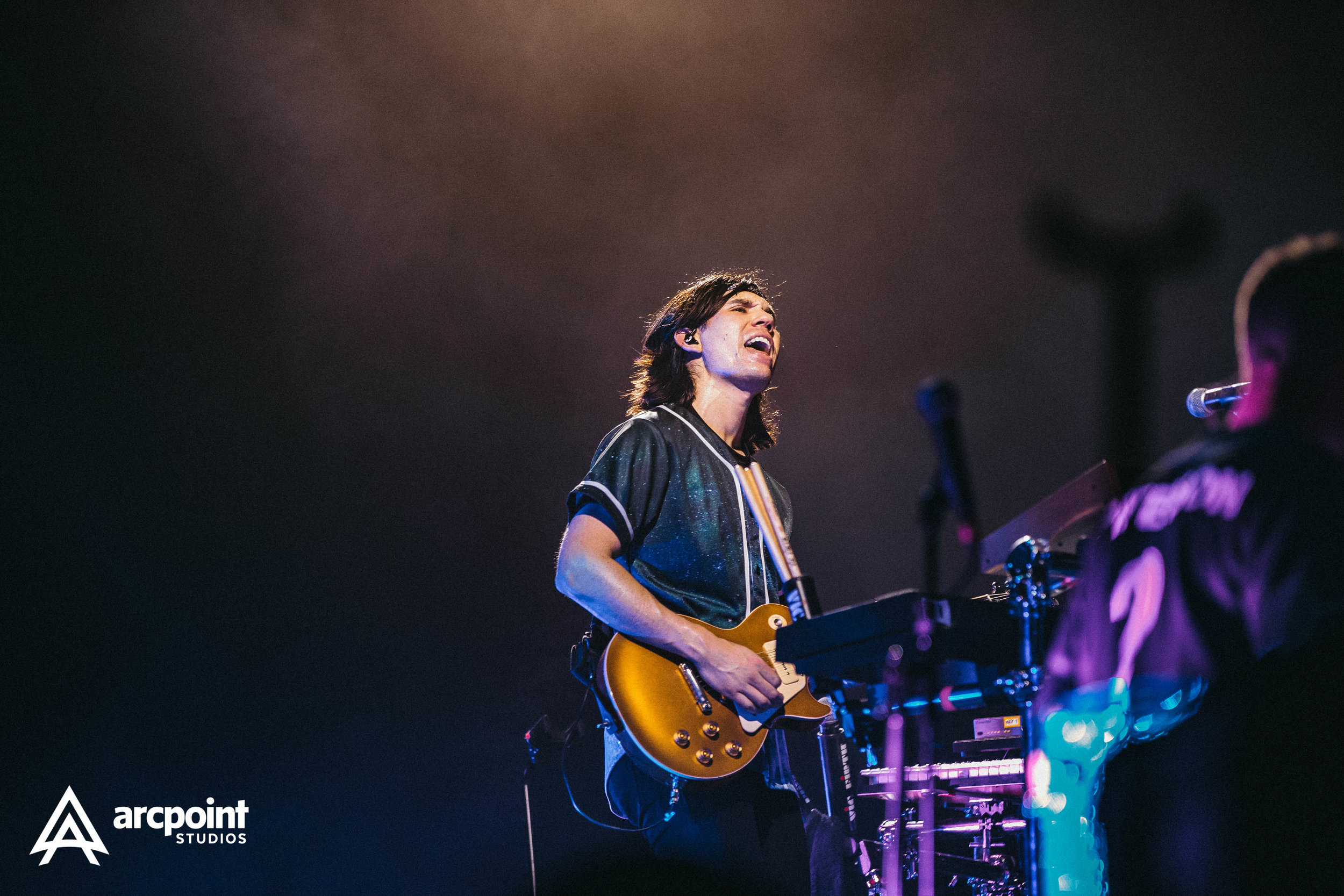 A musician playing an electric guitar during a live concert, singing with eyes closed and a passionate expression, with stage lights illuminating him.