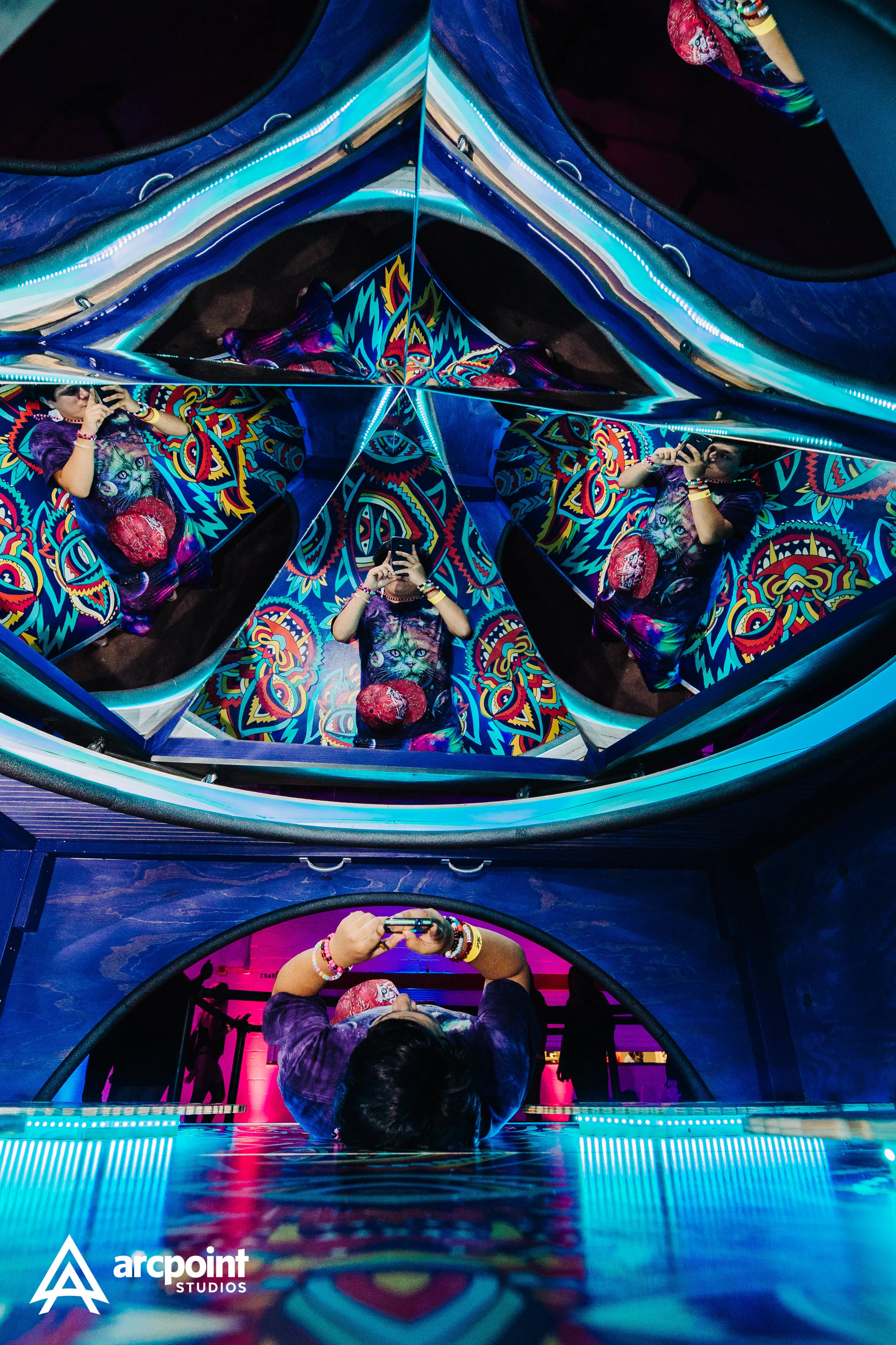 Person taking a selfie in an infinity mirror with colorful psychedelic patterns and multiple reflections.