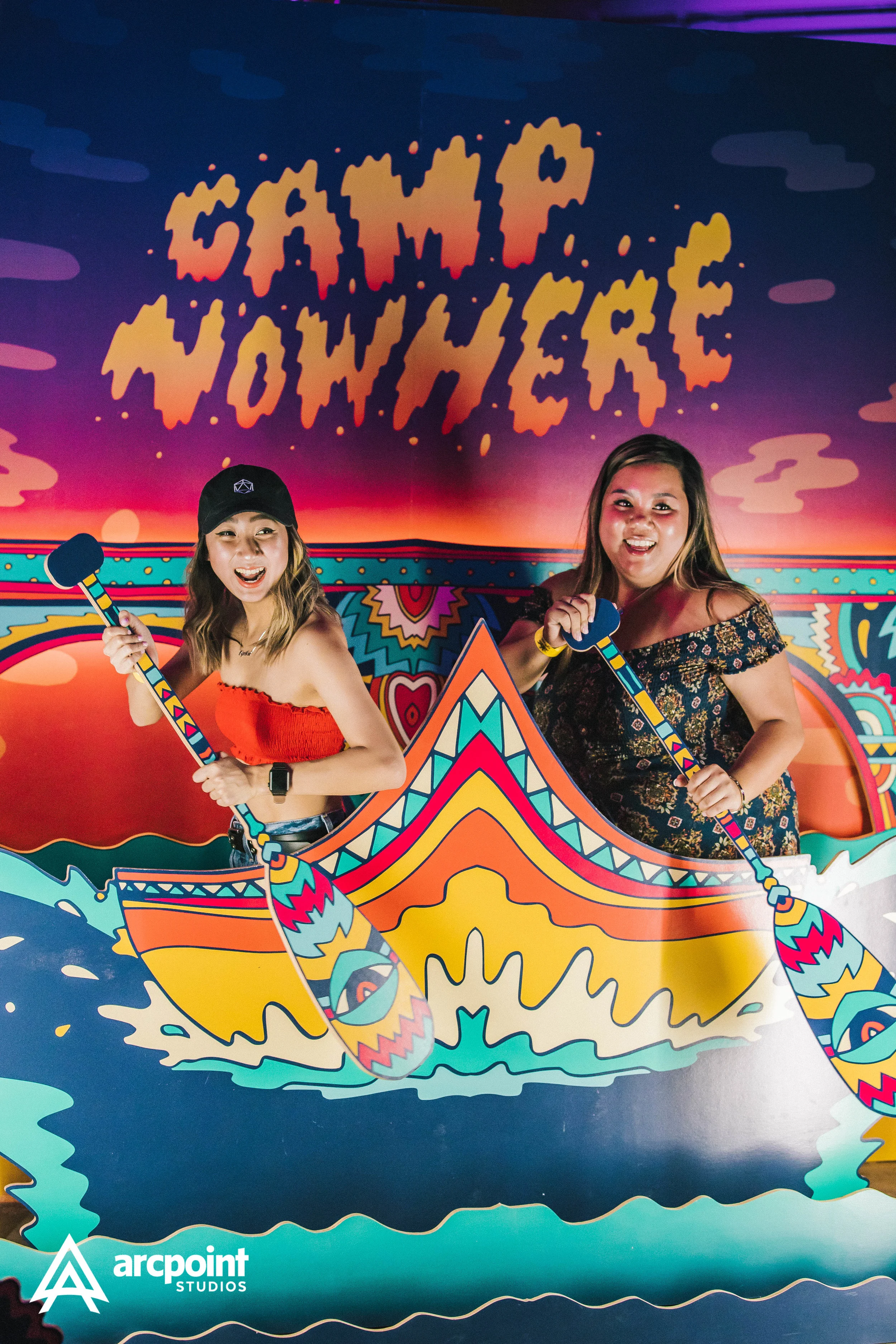 Two women in a colorful boat prop at the Cali Vibes event, with a vibrant background and the words 'CALI VIBES' written above.