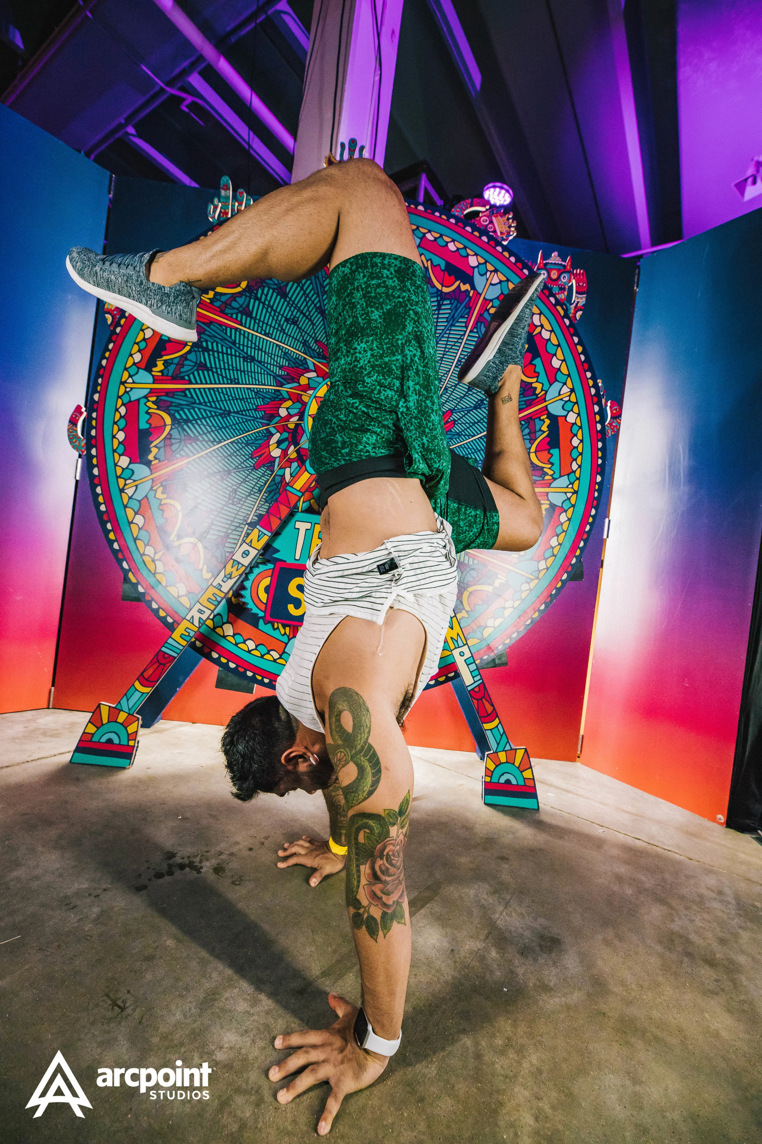 A man performing a handstand in front of a colorful, carnival-themed backdrop with a Ferris wheel design.