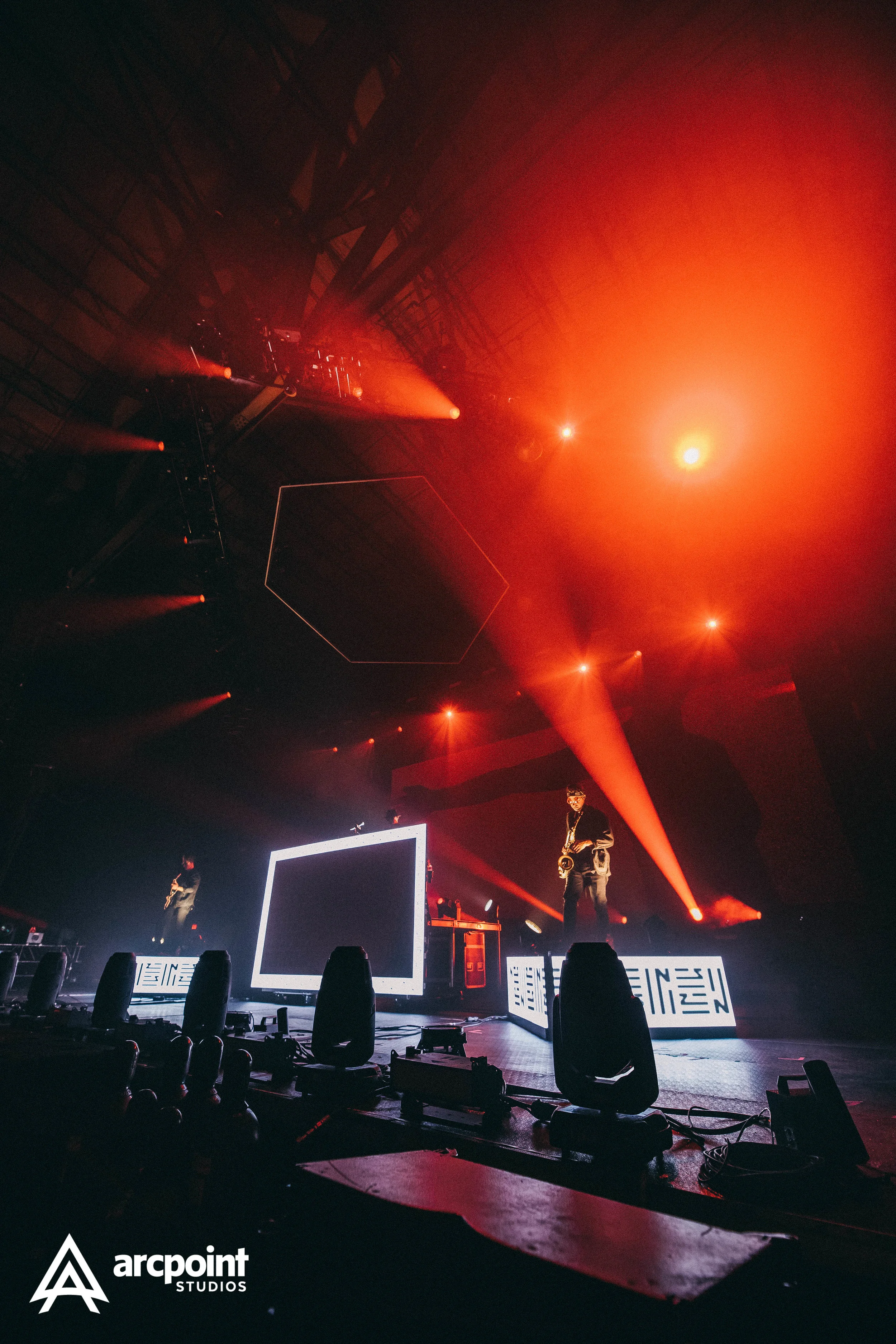 Stage with performers, illuminated by orange and red lights, featuring digital screens and sound equipment, at Arcpoint Studios.